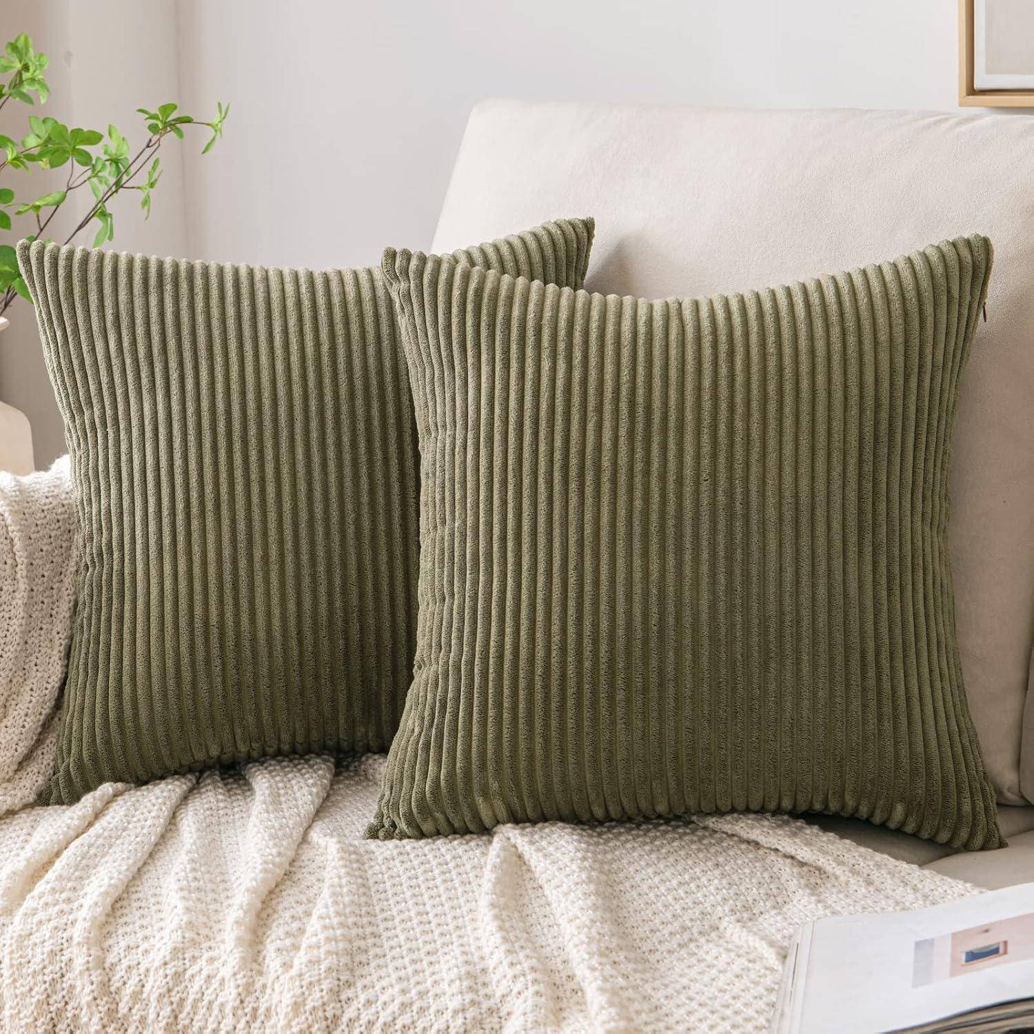 Zwei grüne, gerippte Zierkissen auf einem beigen Sofa, mit einer texturierten cremefarbenen Decke, die über die Armlehne drapiert ist. Eine kleine Topfpflanze ist sichtbar.