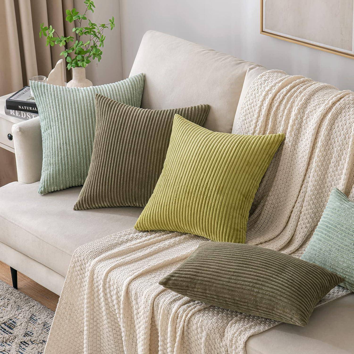 Ein beige Sofa mit einer weichen Decke und mehreren gestreiften Kissen in verschiedenen Grün- und Brauntönen, platziert in einem gemütlichen, sonnendurchfluteten Wohnzimmer.