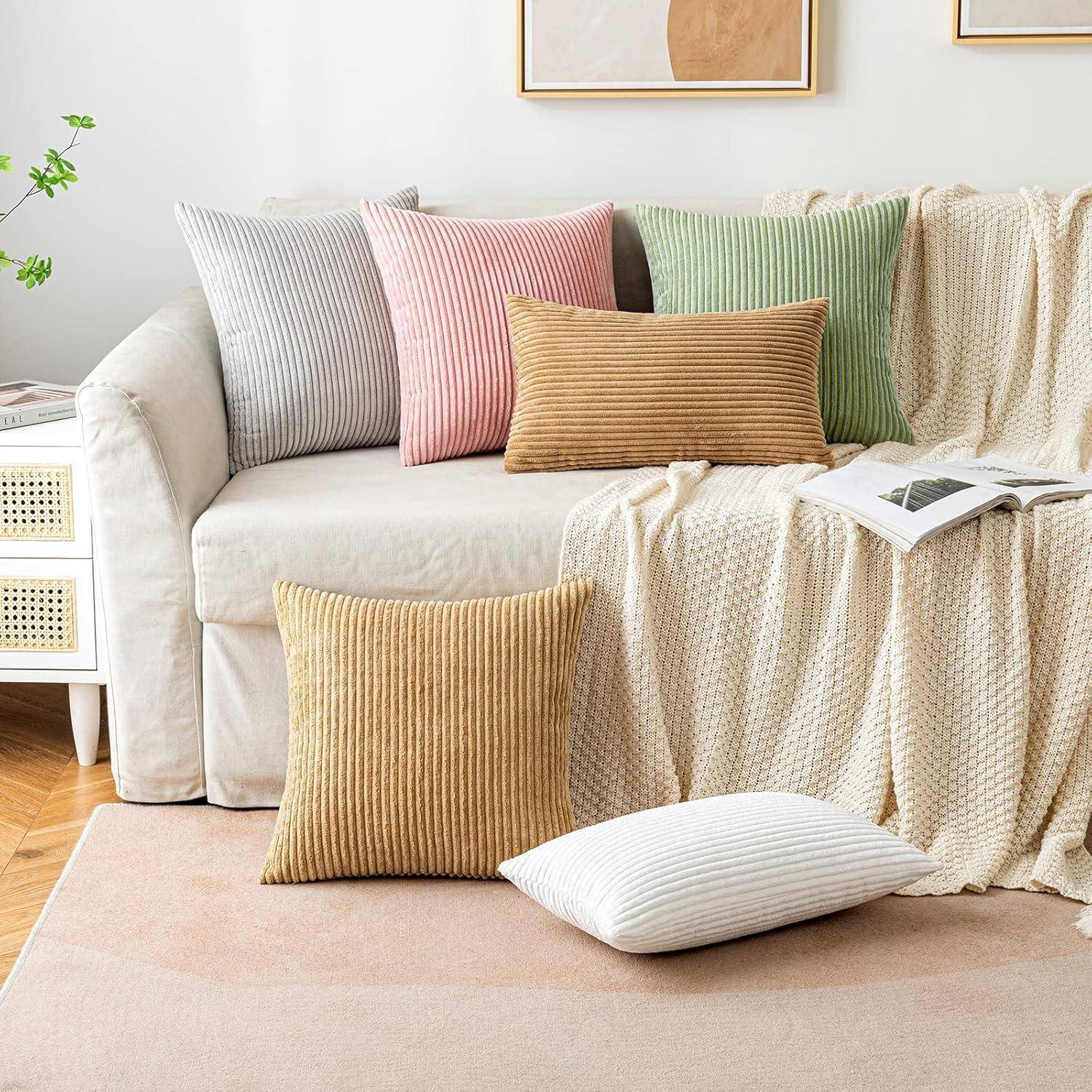 Ein beiger Sofa mit einer strukturierten Decke, verschiedenen gestreiften und einfarbigen Kissen sowie zwei gerahmten abstrakten Kunstwerken an der Wand.