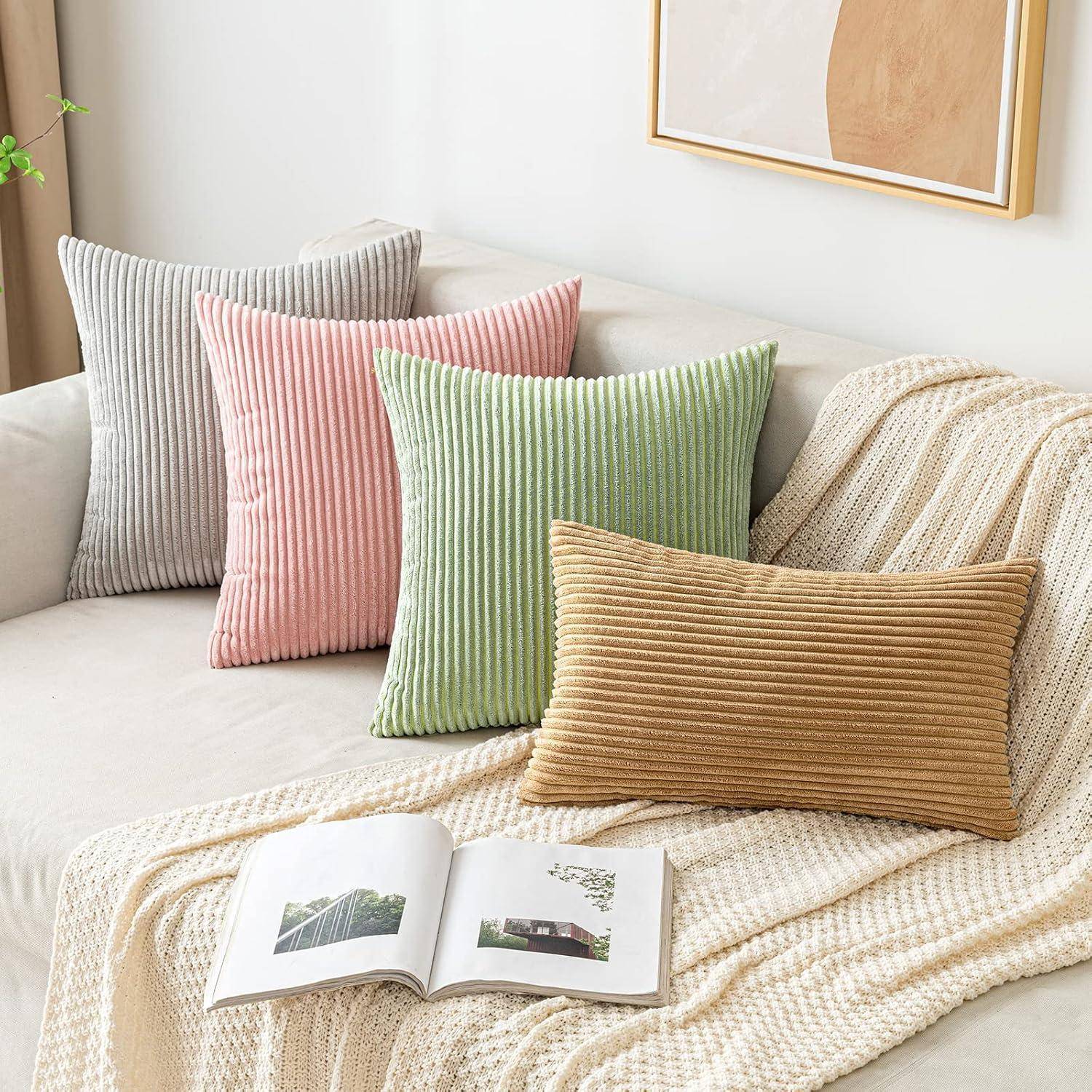Couch mit strukturierten Kissen in verschiedenen Farben; eine beige Decke und ein aufgeschlagenes Buch liegen darauf, während abstrakte Kunst an der Wand hängt.