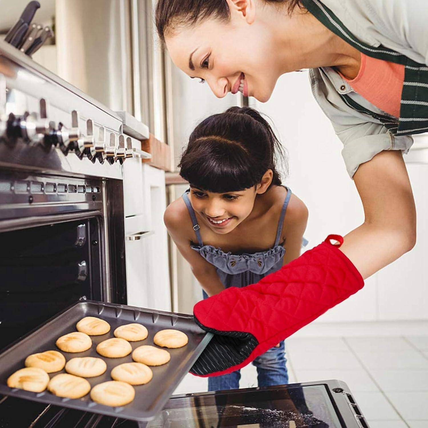 Eine Frau und ein junges Mädchen backen zusammen. Die Frau, die eine Schürze trägt, nimmt ein Backblech mit Keksen aus dem Ofen, während das Mädchen gespannt zuschaut.