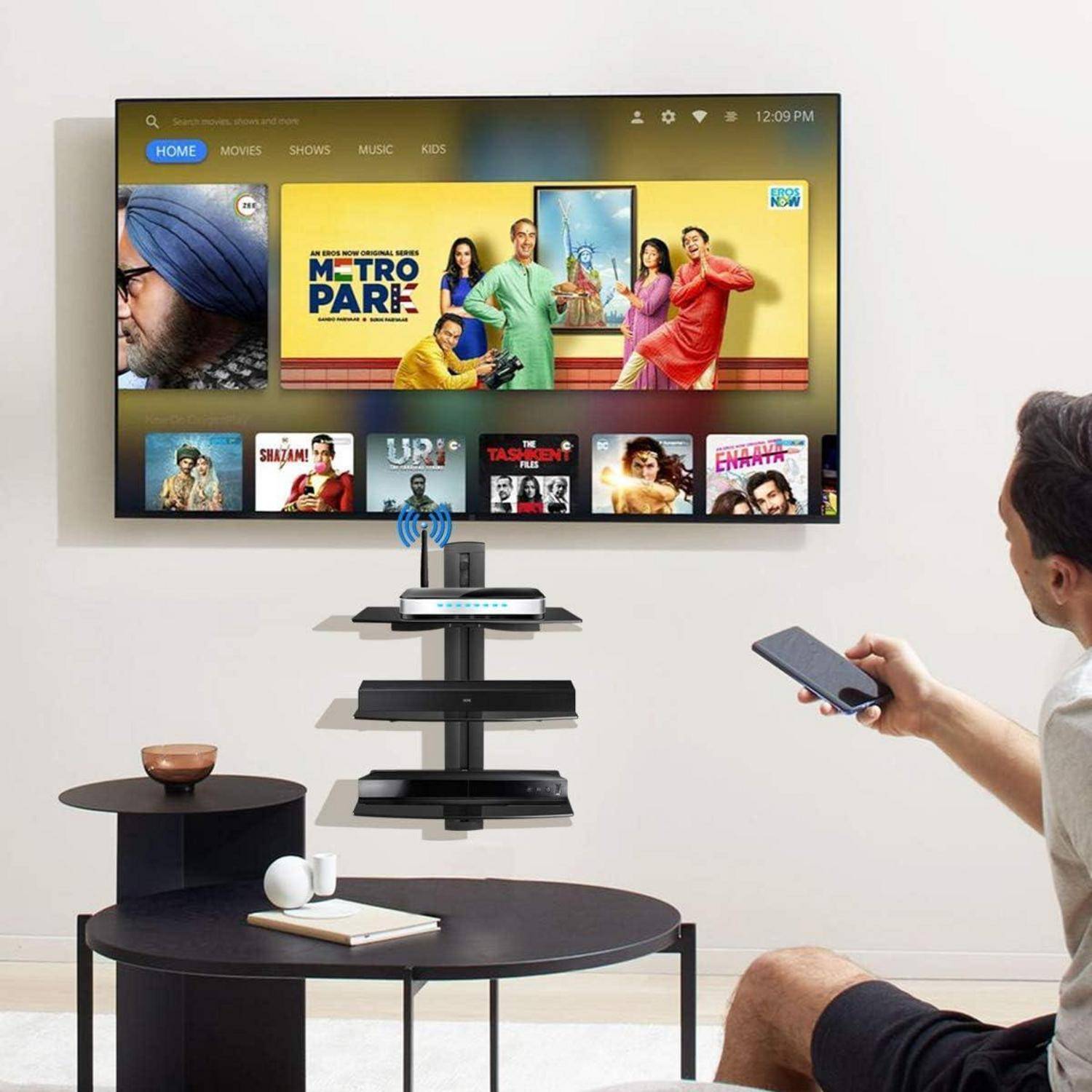 Eine Person, die ein Smartphone benutzt, um mit einem an der Wand montierten Smart-TV zu interagieren, der eine Streaming-Dienst-Benutzeroberfläche mit Film- und Serienoptionen anzeigt.