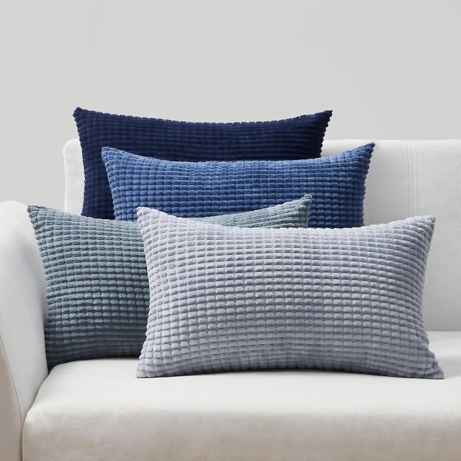 Eine weiße Couch mit vier strukturierten Kissen in Blautönen, die von einem hellen gräulichen Blau bis zu einem dunklen Marineblau reichen, von vorne nach hinten angeordnet.