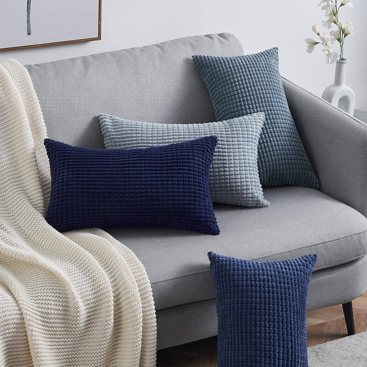 Ein grauer Sofa mit strukturierten Kissen in Blau- und Grautönen, begleitet von einer beigen gestrickten Decke und einer kleinen Topfpflanze auf dem Beistelltisch.