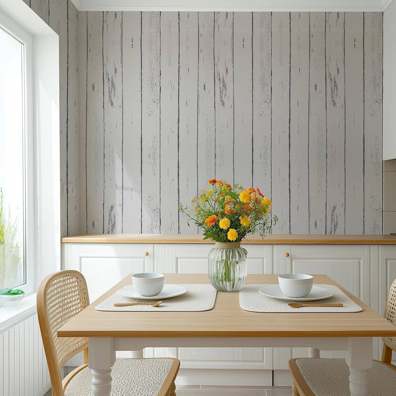 Ein Essbereich mit einem Holztisch, der für zwei Personen gedeckt ist, mit einer Vase voller bunter Blumen. Licht strömt durch ein Fenster und beleuchtet den Raum.