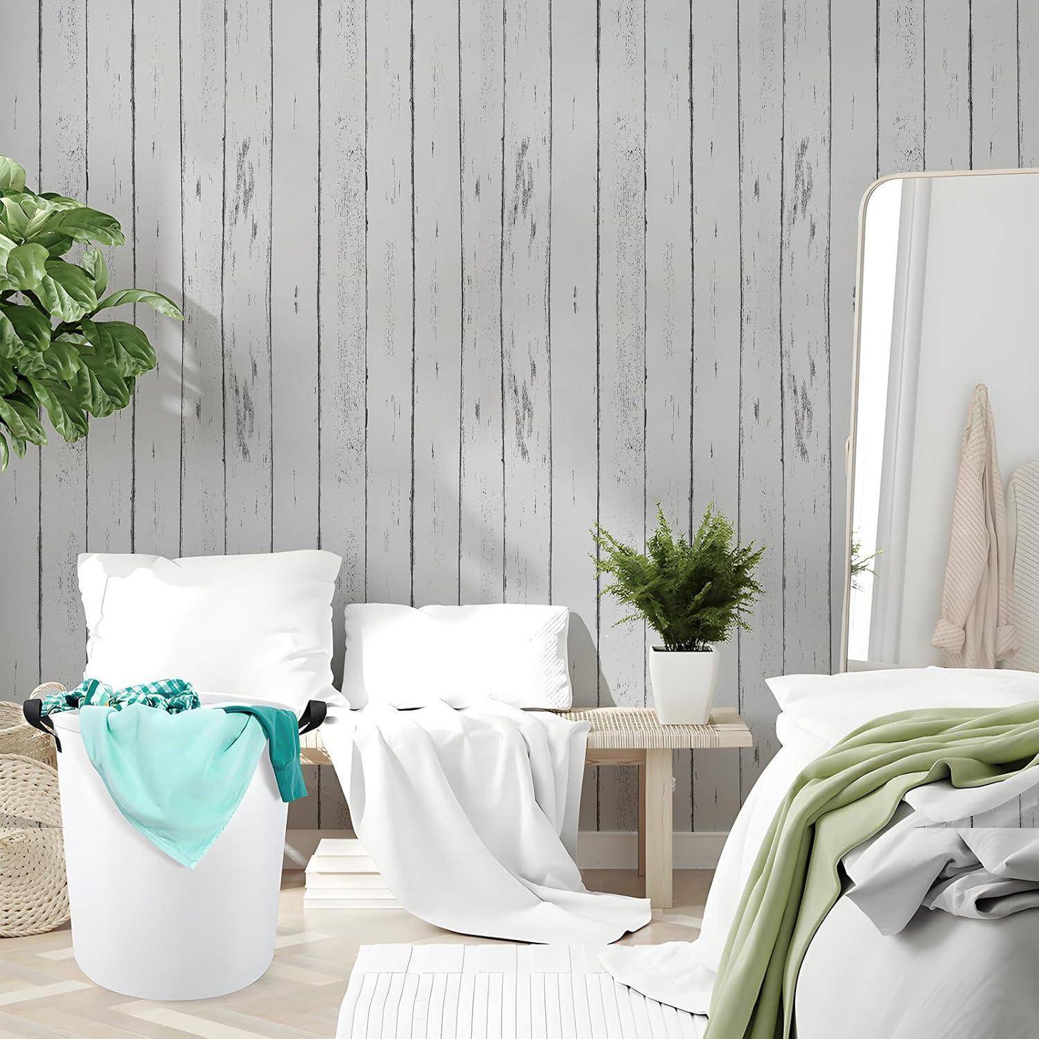 Ein gemütliches, minimalistisches Schlafzimmer mit einer Holzvertäfelungswand, einem Bett mit weißer Bettwäsche, einem Korbwäschekorb und Zimmerpflanzen als Dekoration.