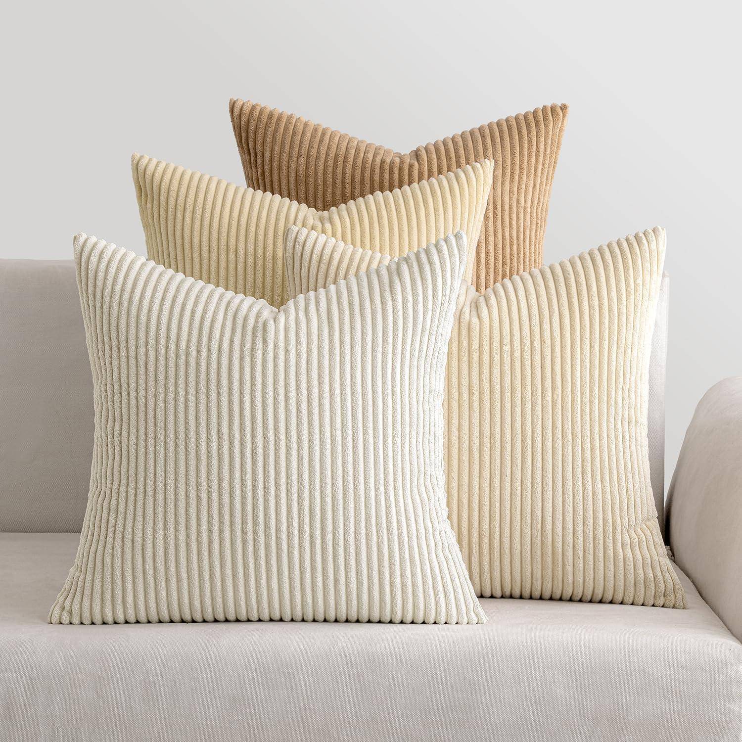 Drei strukturierte Kissen in Beige, Elfenbein und Creme sind auf einem beigen Sofa angeordnet. Die Umgebung ist minimalistisch mit neutralen Tönen.