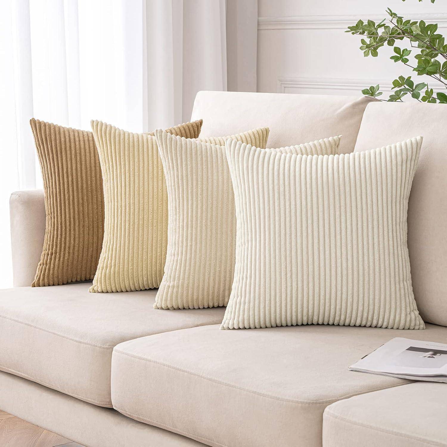Vier strukturierte Kissen in neutralen Farbtönen, die auf einem beigen Sofa angeordnet sind, wobei eine blattreiche Pflanze in der oberen rechten Ecke Grün hinzufügt.