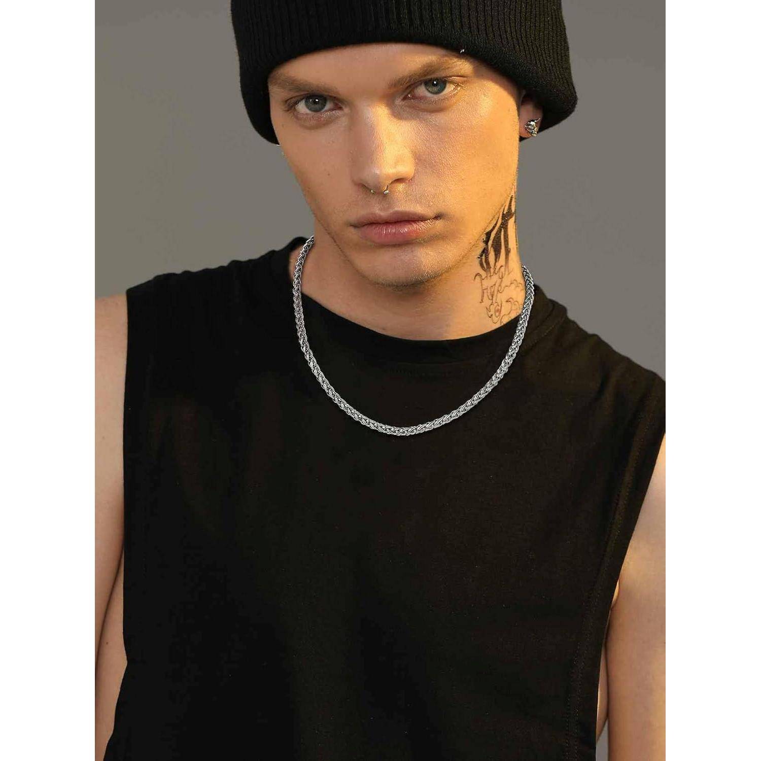 Eine Person mit schwarzer Beanie und ärmelloser Bluse blickt direkt in die Kamera. Sie trägt eine Halskette und hat ein sichtbares Halstattoo.