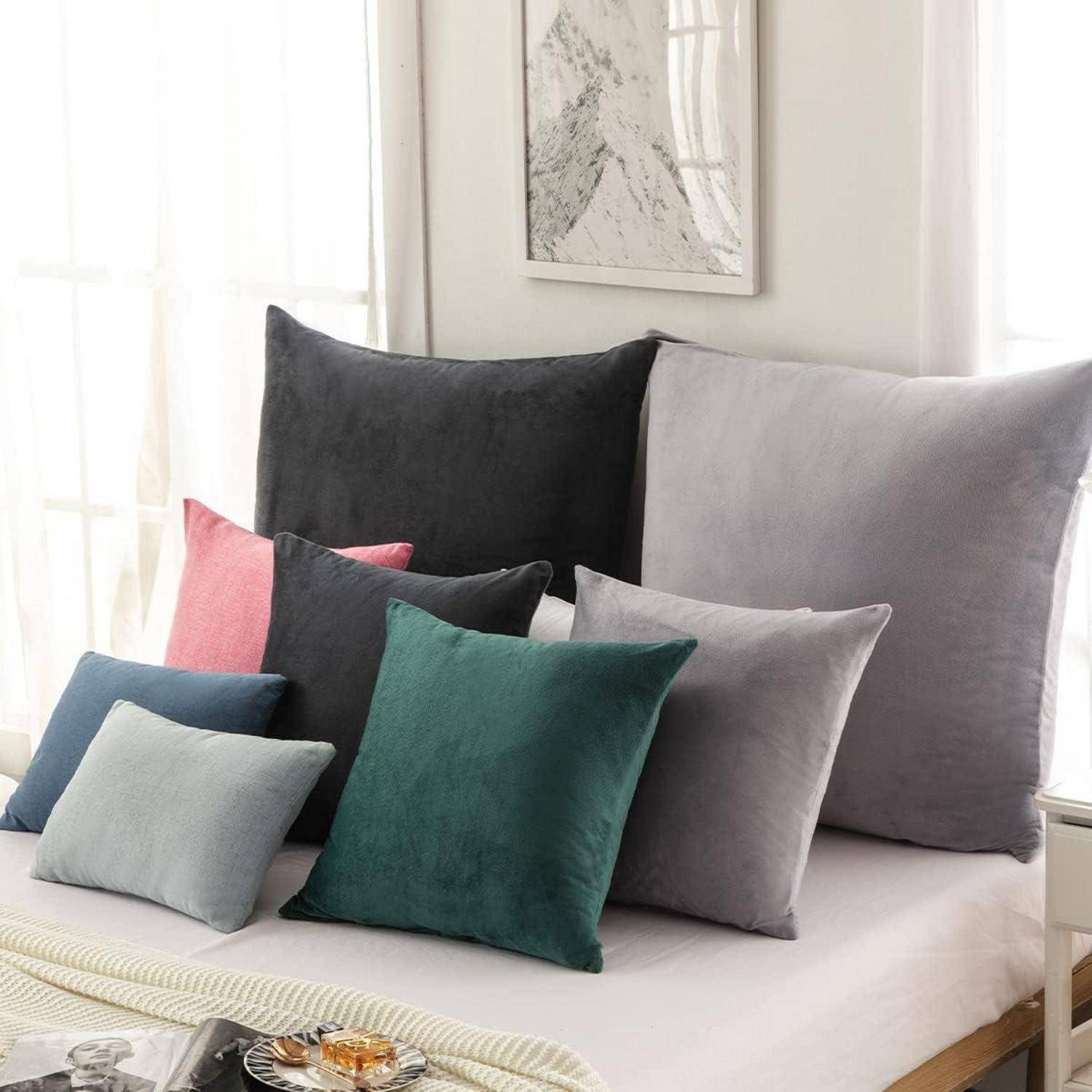 Ein Bett, geschmückt mit Kissen in verschiedenen Größen in den Nuancen von Grau, Rosa, Grün und Blau, vor einem Hintergrund von lichtdurchlässigen, weißen Vorhängen.