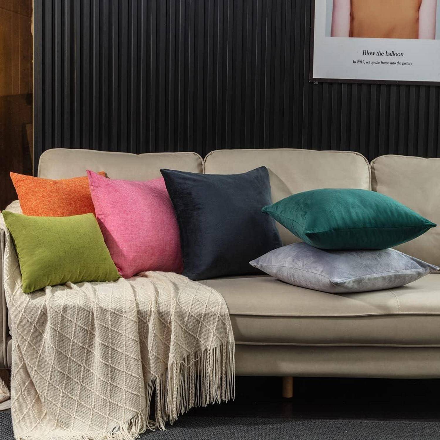 Ein beige Sofa mit einer Vielzahl bunter Kissen steht vor einer dunklen Holzvertäfelung. Eine cremefarbene Decke ist über eine Armlehne drapiert.