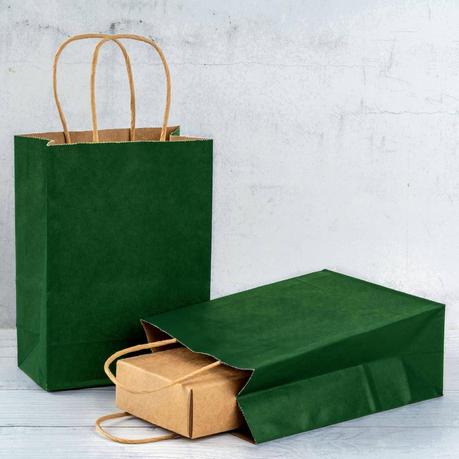 Eine stehende grüne Papiertüte mit Griffen steht neben einer ähnlichen Tasche, die flach auf einer grauen Oberfläche liegt und damit auf Einkaufen oder Geschenkverpackung hinweist.