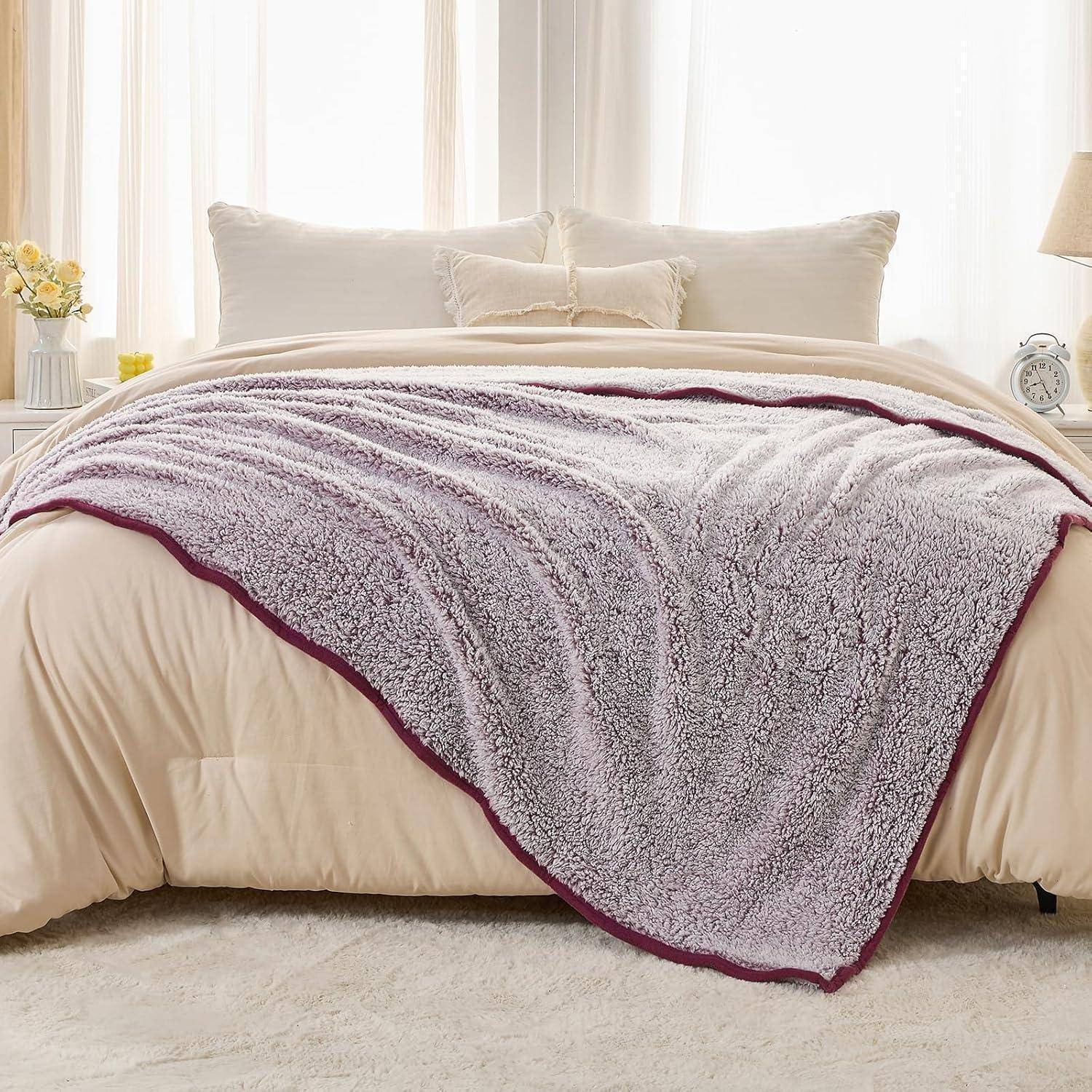 Ein gemütliches Schlafzimmer mit einem sorgfältig aufgemachten Queensize-Bett, das mit einer weichen, strukturierten grauen Decke mit bordeauxrotem Rand unter sanftem Tageslicht versehen ist.