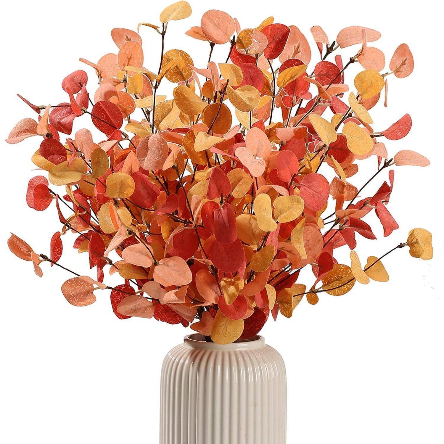 Ein Blumenstrauß aus leuchtend roten, orangefarbenen und gelben Blättern in einer weiß gerippten Vase, der eine Herbststimmung heraufbeschwört.