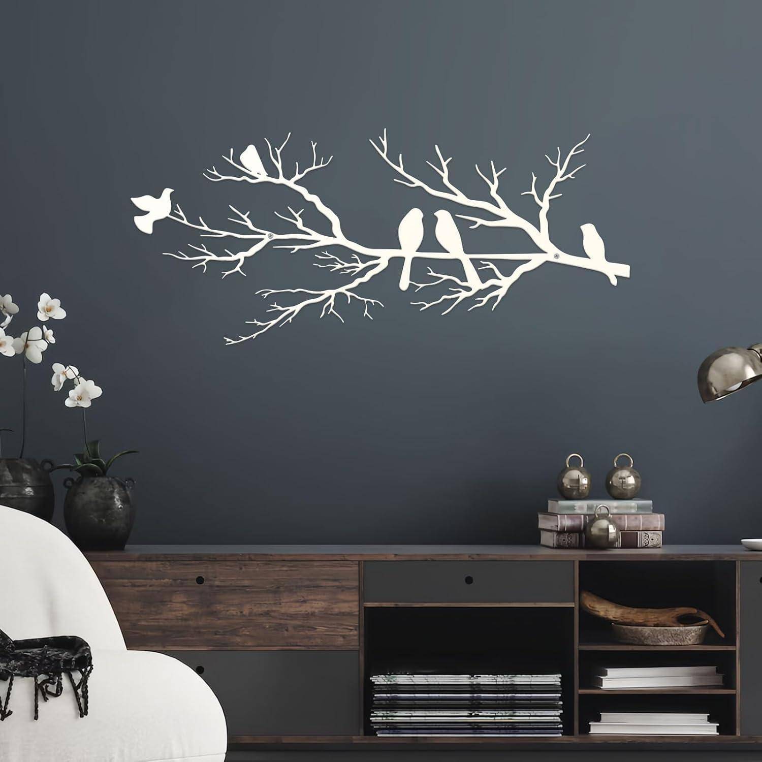 Ein minimalistisches Zimmer mit einer grauen Wand zeigt ein Kunstwerk mit einem weißen Ast und Vögeln. Ein weißer Stuhl, Topfpflanzen und eine Holzkonsole sind zu sehen.