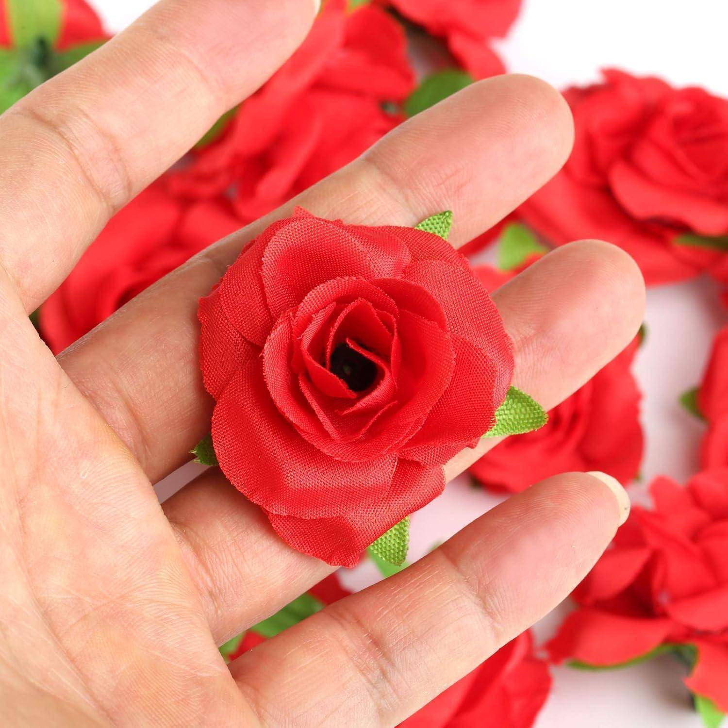 Eine Hand, die eine einzelne kleine rote Stoffrose mit grünen Blättern hält, umgeben von ähnlichen Stoffrosen im Hintergrund.