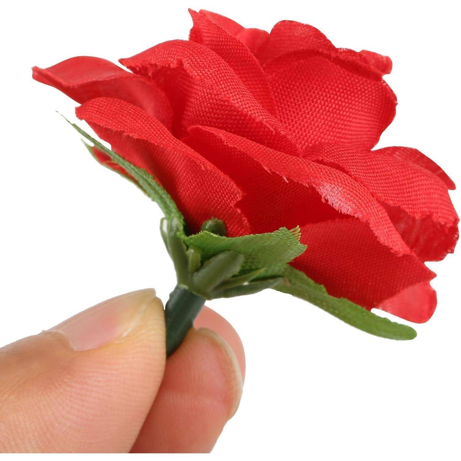 Eine Hand hält eine kleine, rote künstliche Rose mit grünen Blättern, von der Seite betrachtet vor einem weißen Hintergrund.