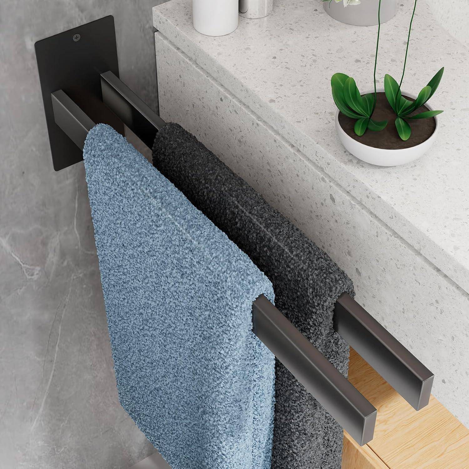 Ein wandmontiertes Handtuchhalter hält ein blaues und ein graues Handtuch. Eine kleine grüne Pflanze in einem weißen Topf steht auf der Arbeitsplatte in der Nähe.