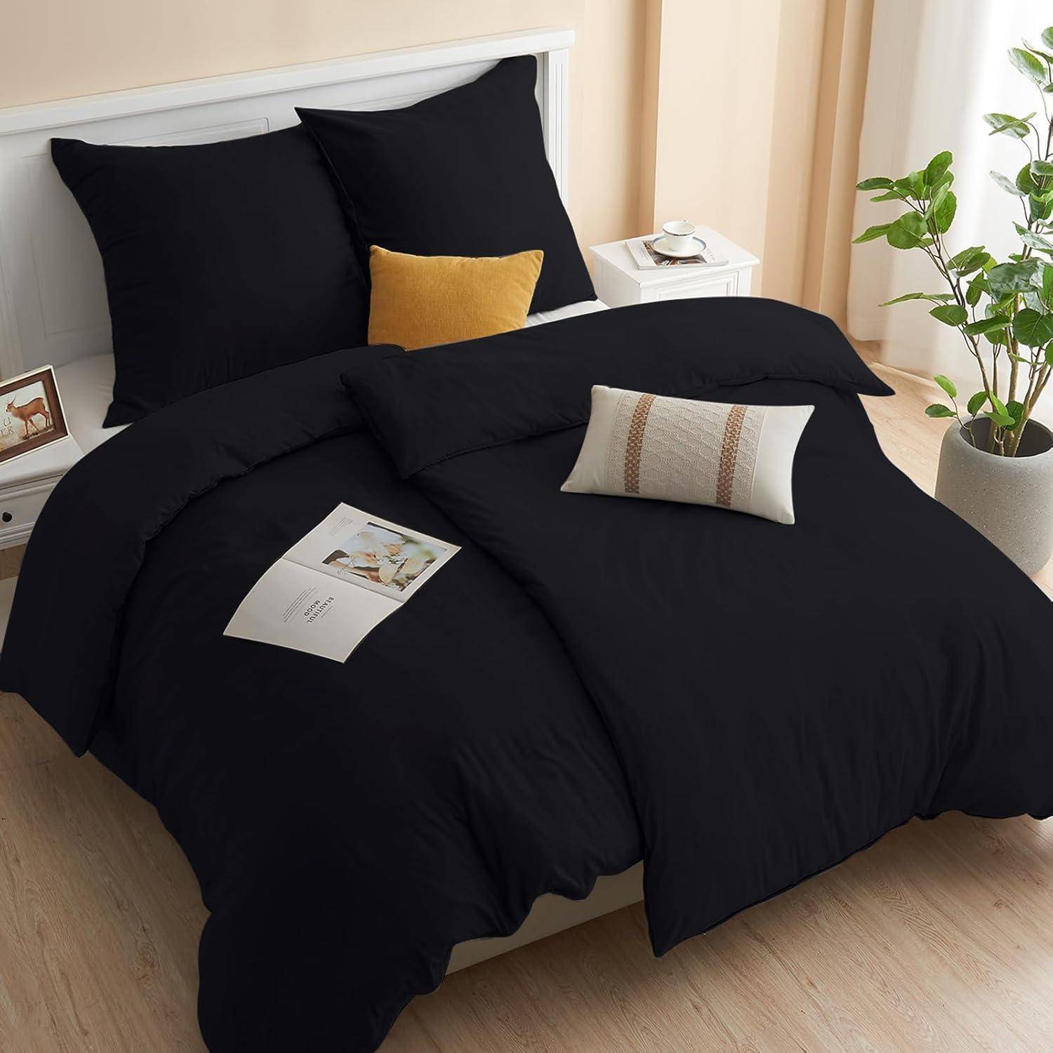 Ein ordentlich gemachtes Bett mit schwarzer Bettwäsche, zwei Kissen und einem Zierkissen. Eine Zeitschrift und eine Pflanze stehen auf weißen Nachttischen.