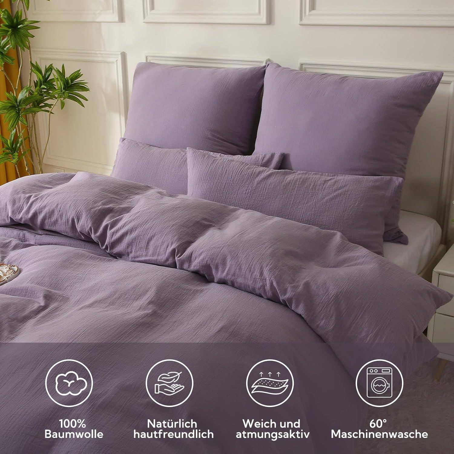 Ein Bett mit Lavendel-Bettwäsche, einschließlich Kissen und Bettdecke, wird gezeigt. Symbole darunter zeigen an, dass das Material zu 100% Baumwolle ist, naturfreundlich, atmungsaktiv und bei 60°C maschinell waschbar.