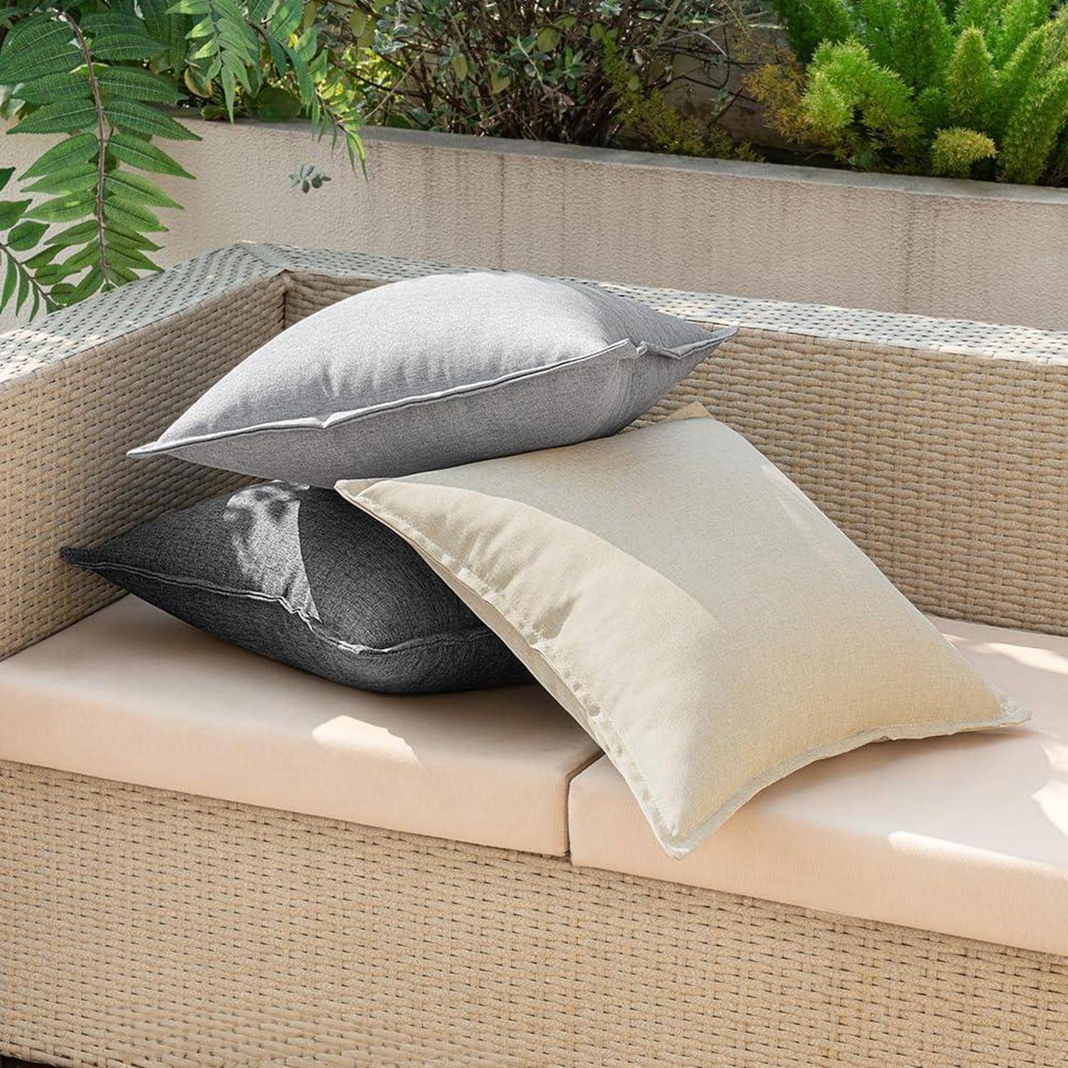 Outdoor-Gartenmöbel-Set mit beigen Kissen und drei dekorativen Zierkissen in Grau, Dunkelgrau und Creme, vor einer Gartenkulisse platziert.