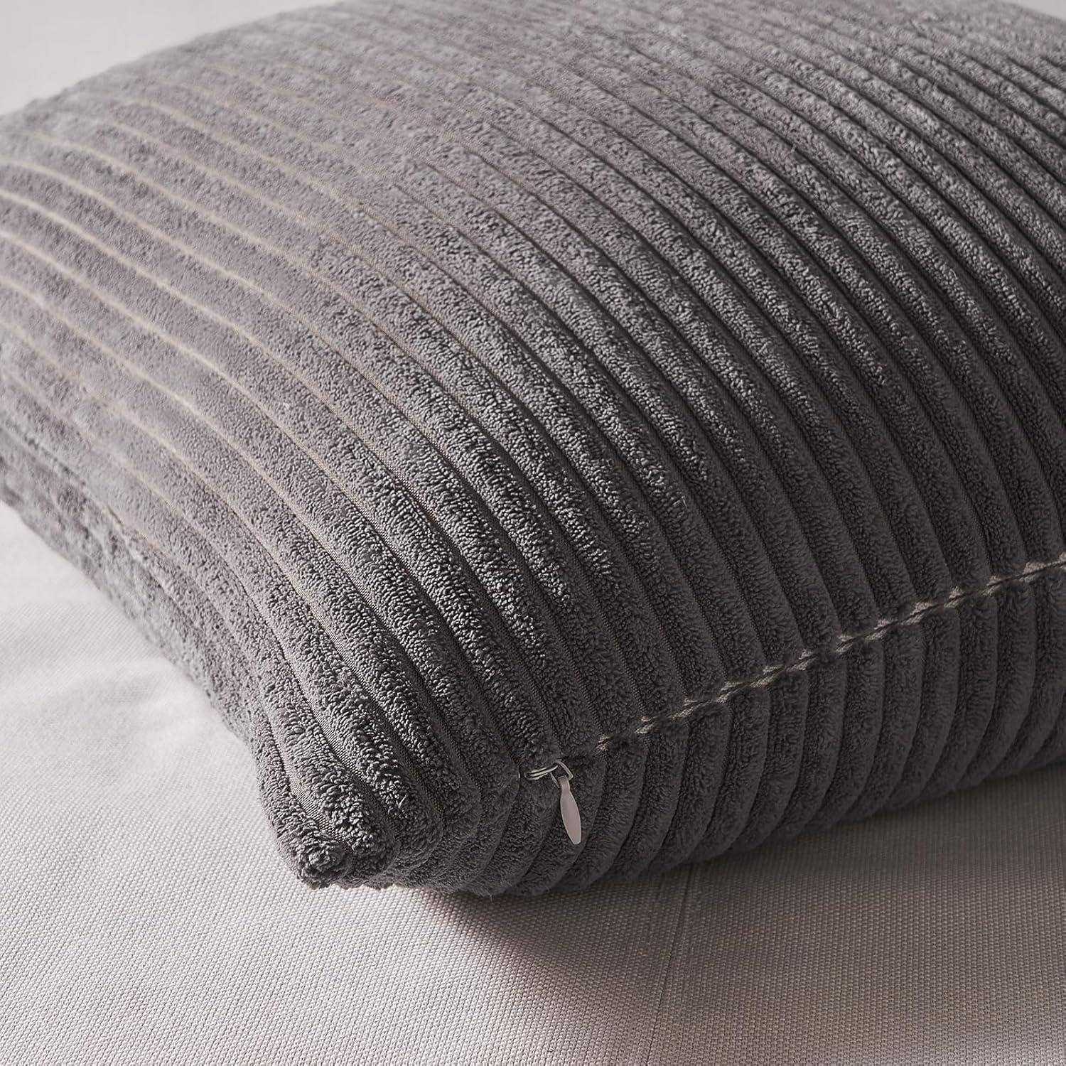 Ein grauer, gerippter Kopfkissen auf einer hellen Stoffoberfläche, der ein modernes, gemütliches Design präsentiert.