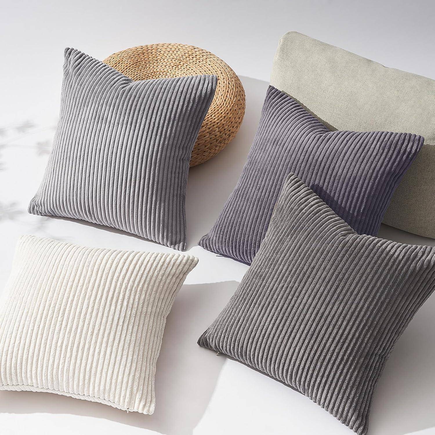 Vier strukturierte Kissen in Grau, Creme und Braun sind auf einer hellen Oberfläche mit weichen Schatten angeordnet und betonen Komfort und Stil.