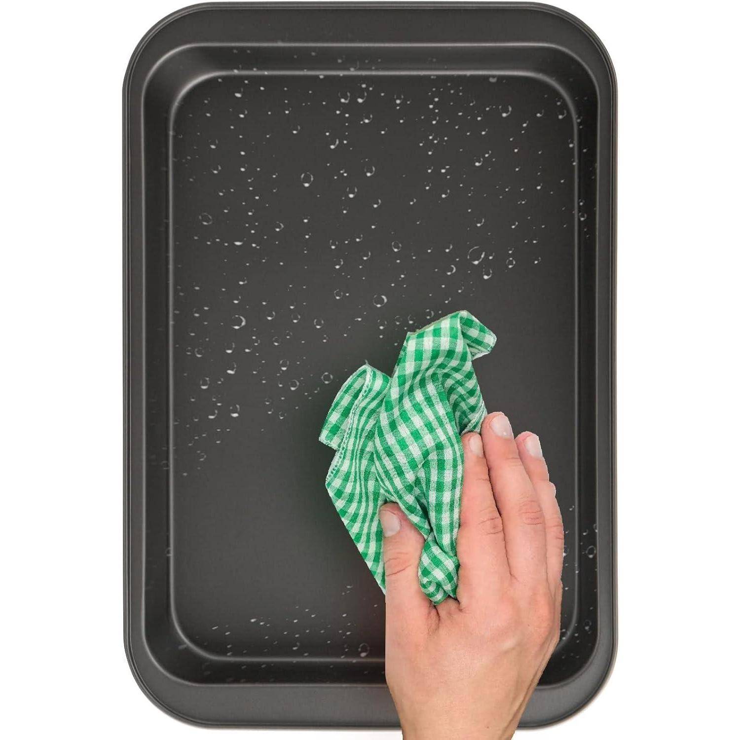 Eine Hand reinigt ein nasses Backblech mit einem grün-weiß kariertem Tuch.