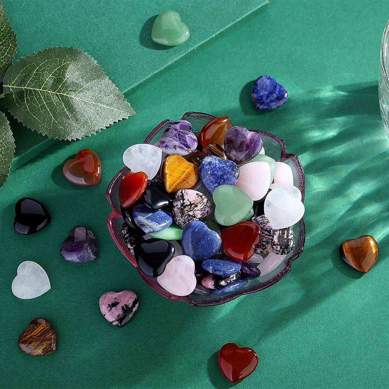 Eine kleine Zierschale, gefüllt mit bunten, herzförmigen Steinen, darunter Amethyst und Jade, ruht auf einem grünen Stoff mit verstreuten Blättern.