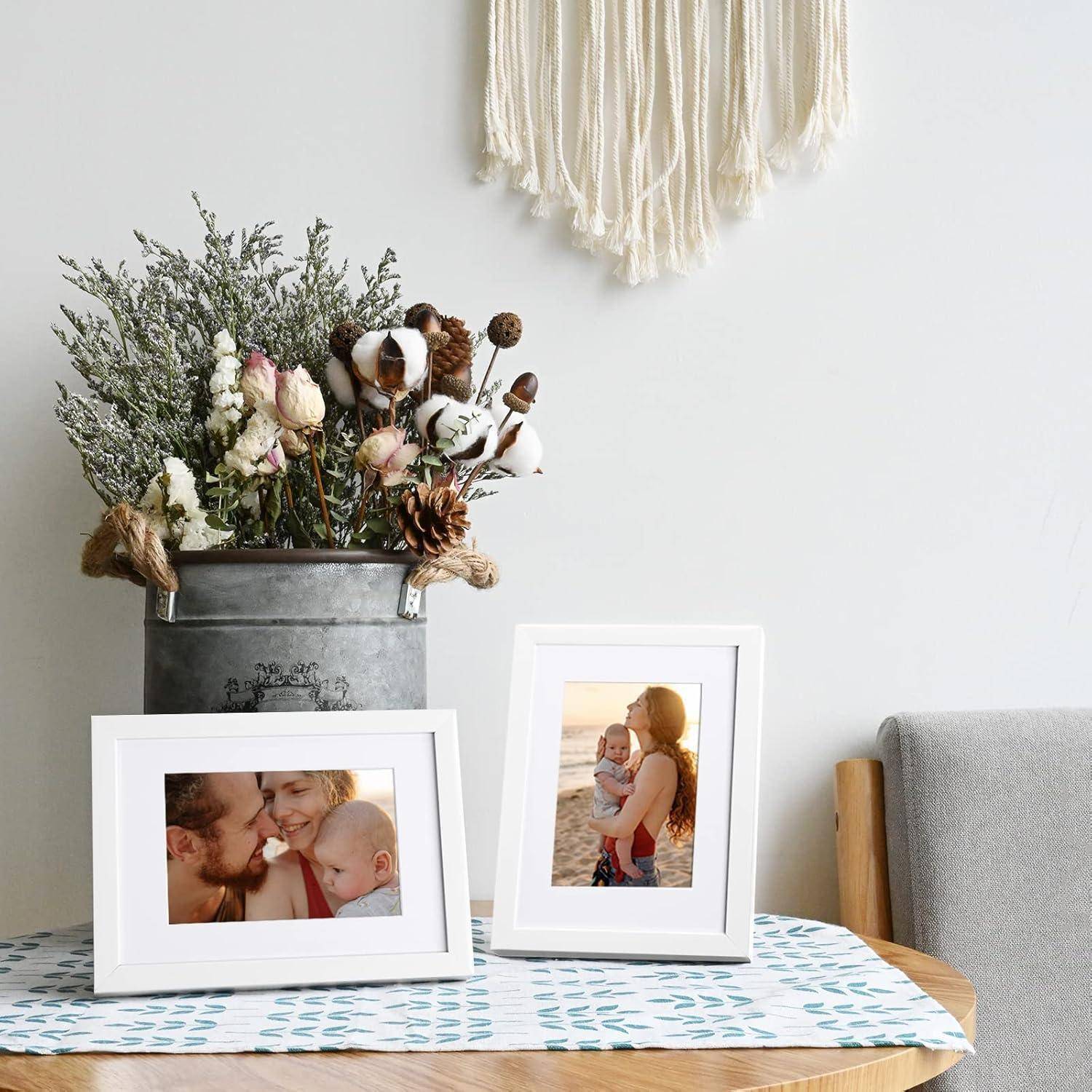 Zwei gerahmte Bilder einer glücklichen Familie auf einem Tisch mit einer Blumenarrangement in einem Metalleimer. Ein gewebter Wandbehang befindet sich im Hintergrund.