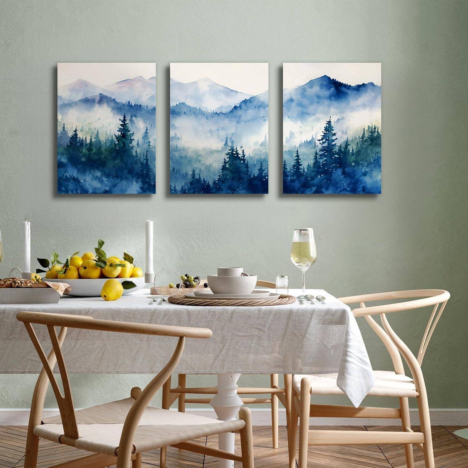 Drei Aquarellgemälde von nebligen Bergen und Wäldern hängen über einem Esstisch, der mit Früchten, Geschirr und zwei Weingläsern gedeckt ist.
