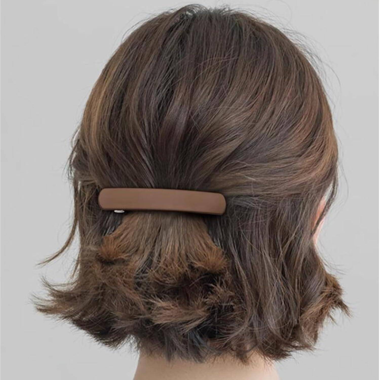 Eine Person mit kurzen, gewellten braunen Haaren wird von hinten gezeigt. Die Haare sind mit einer braunen Haarspange befestigt.