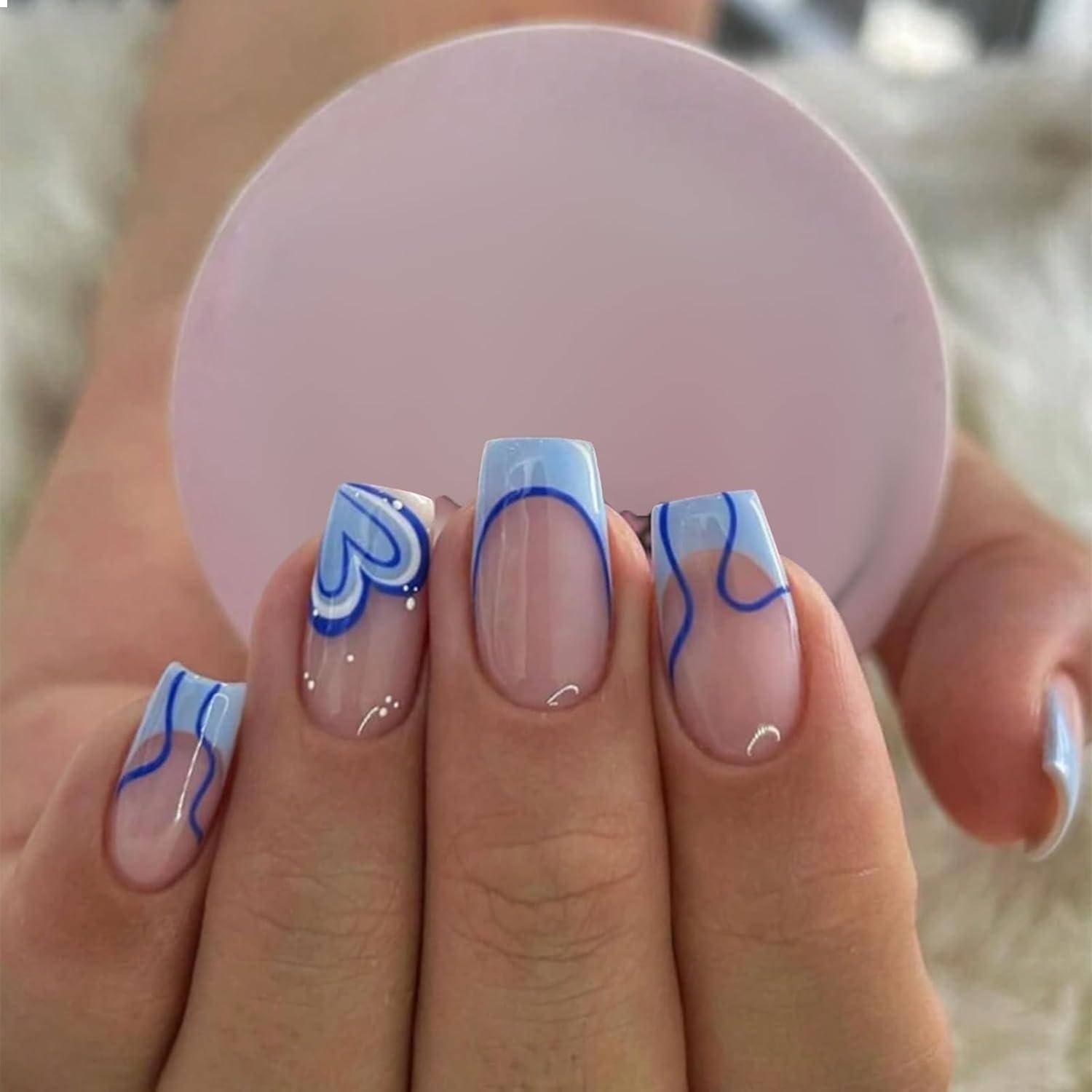 Eine Hand mit Nägeln, die in blauen und weißen abstrakten Mustern lackiert sind, hält ein rundes, pastellrosa Objekt. Der Hintergrund ist unscharf und neutral.