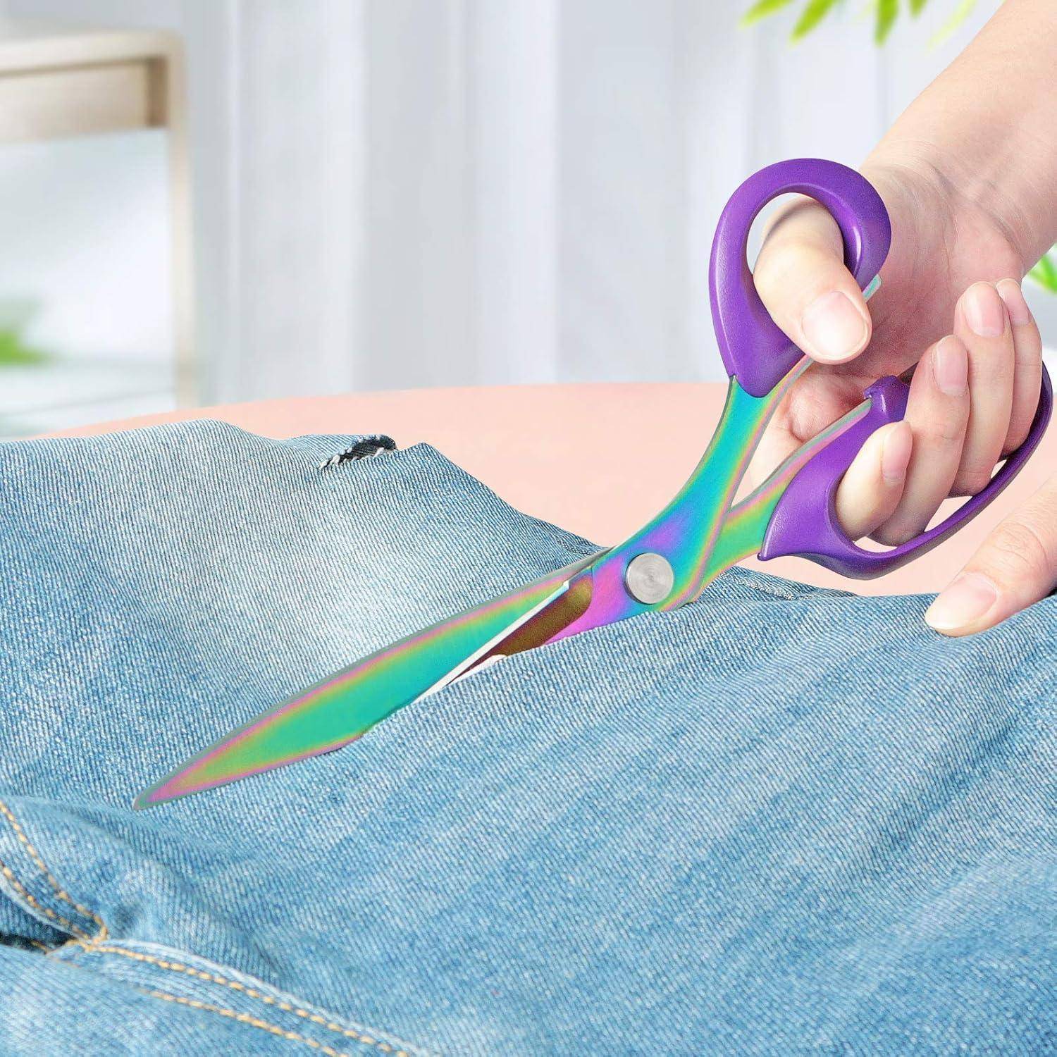 Eine Hand verwendet bunte Schere, um blauen Jeanssstoff zu zerschneiden.