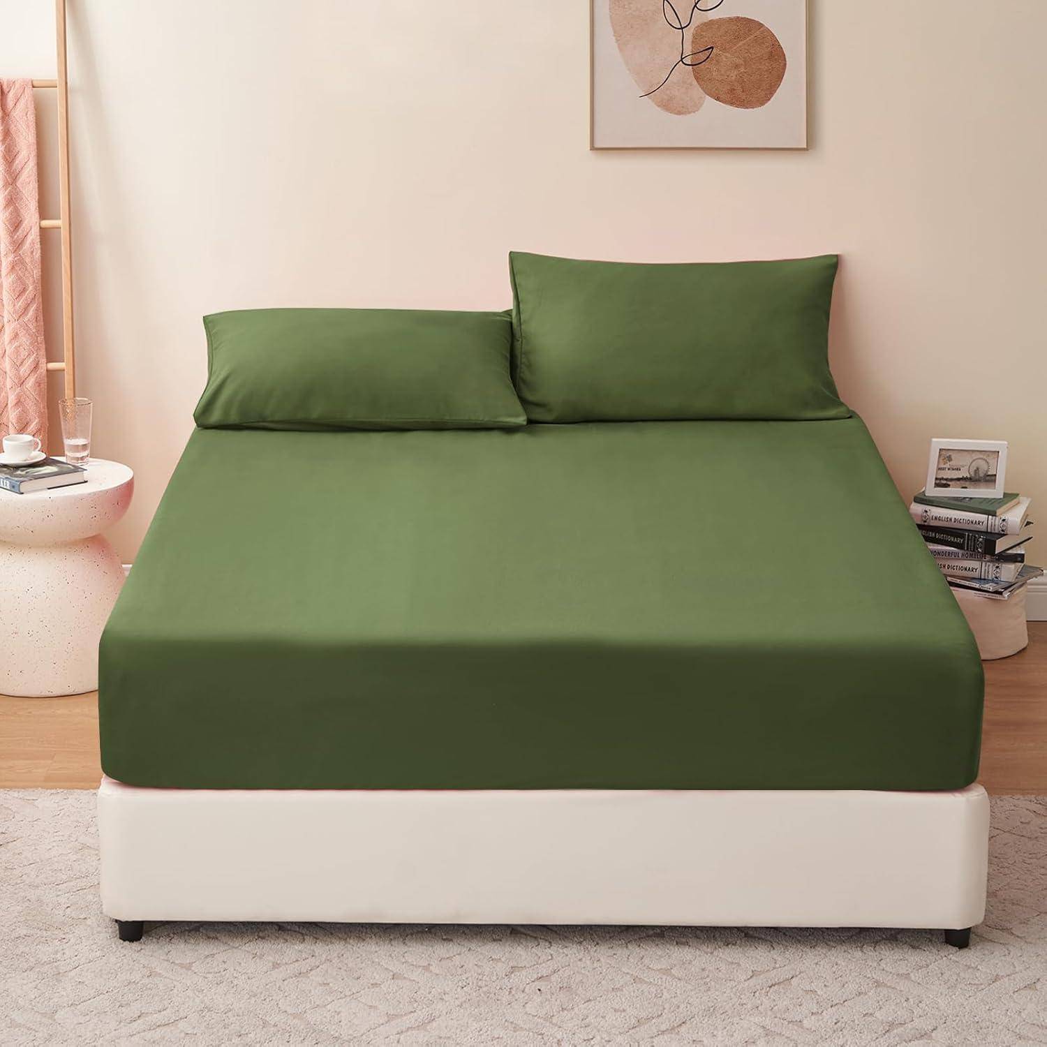 Ein Bett mit grüner Bettwäsche, zwei passenden Kissen, einer weißen Basis und einem rosa Nachttisch mit Gläsern und Büchern. Wandkunst über dem Bett.