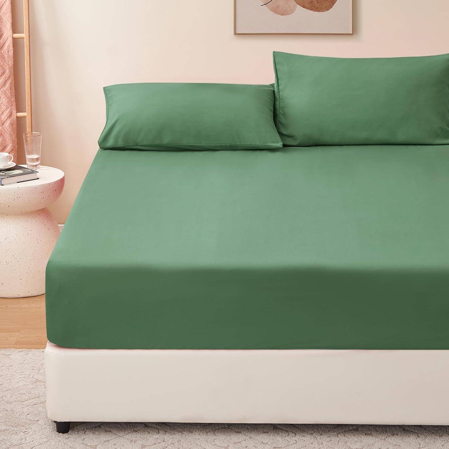 Grünes Bettwäscheset auf einem ordentlich gemachten Bett mit zwei Kissen, neben einem runden Beistelltisch mit einem Glas und einem Buch, in einer gemütlichen Raumgestaltung.