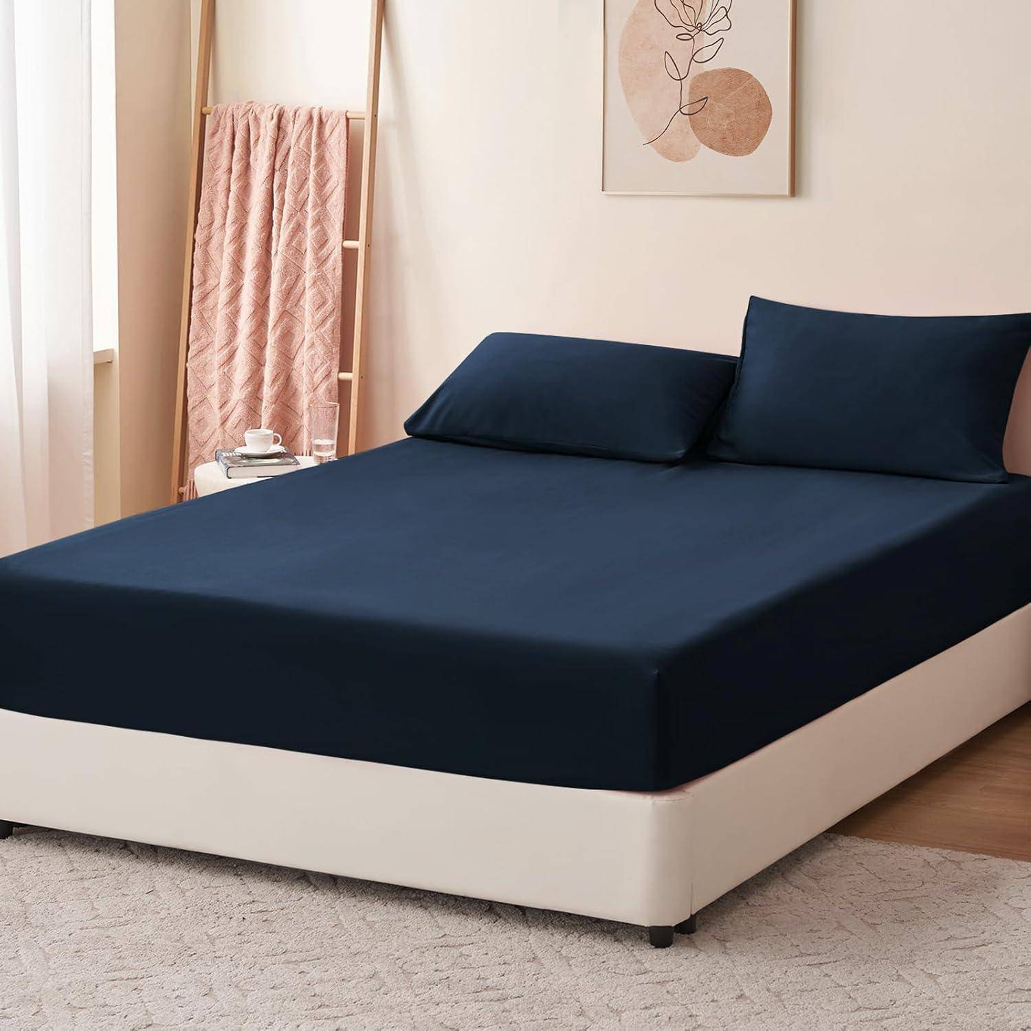 Ein ordentlich gemachtes Bett mit einem dunkelblauen Spannbettlaken und Kissenbezügen, platziert in einem hellen Raum mit einem Holzleiter-Regal und abstrakter Wandkunst.