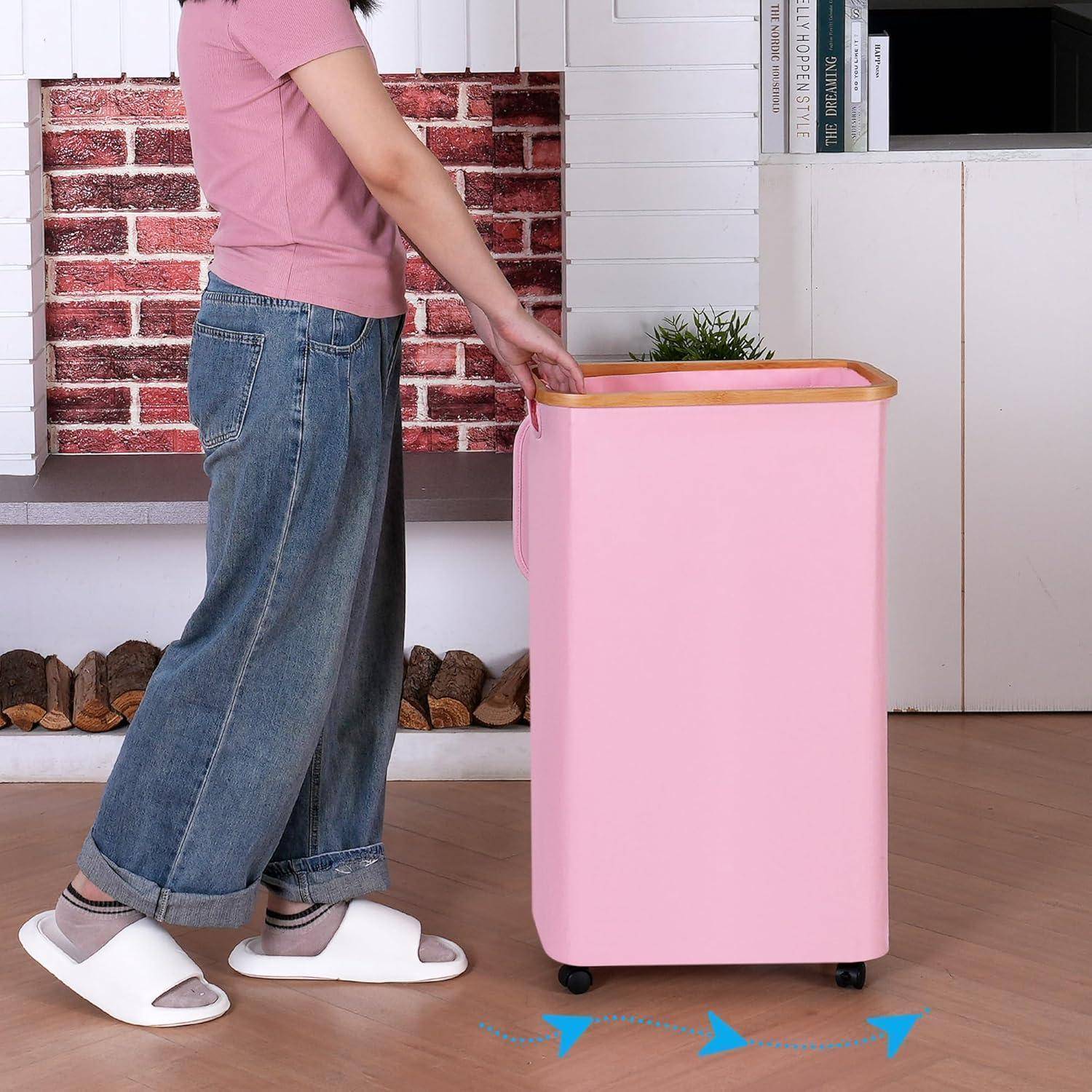 Eine Person in Freizeitkleidung schiebt einen rosa, rollbaren Wäschekorb mit Holzdeckel in einem Raum mit Ziegelmuster und Holzelementen.