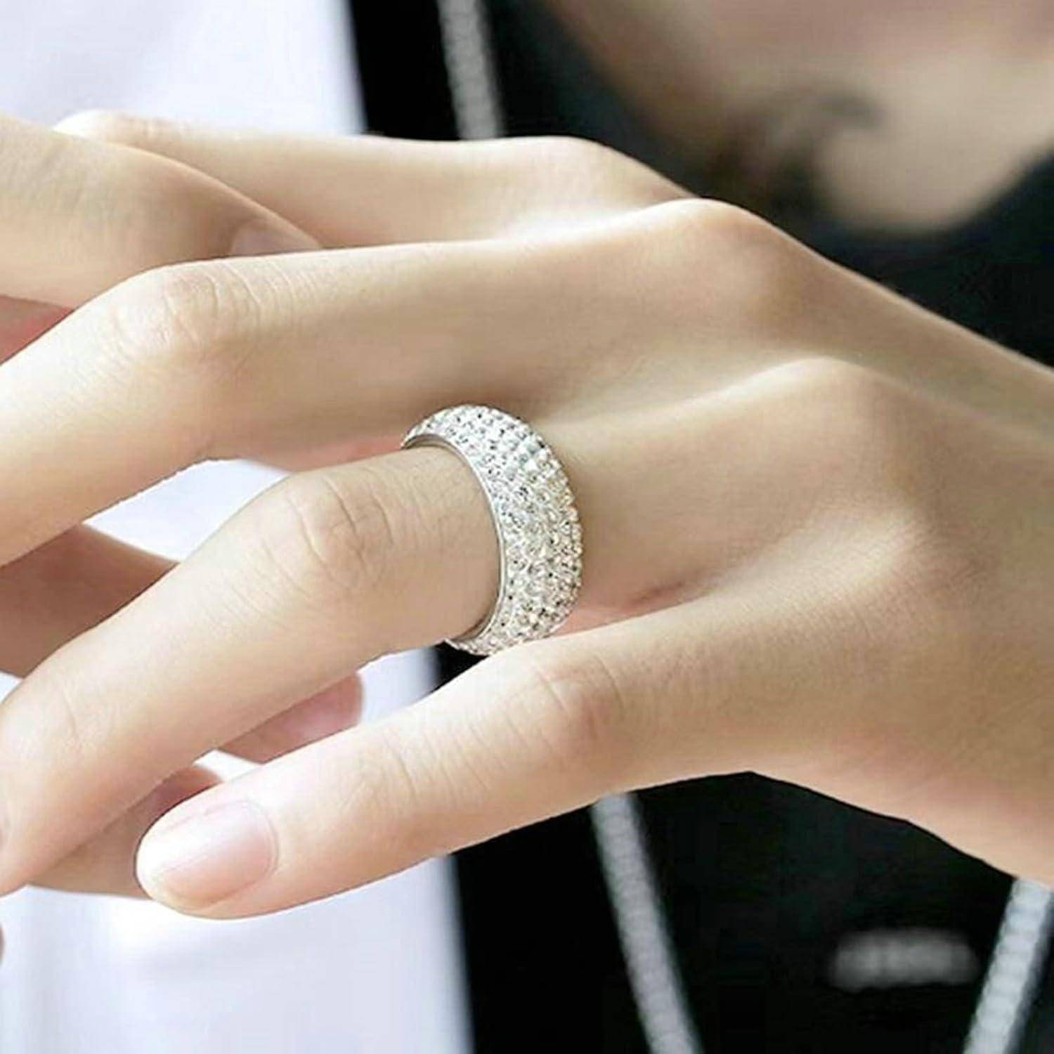 Eine Hand mit einem mit Diamanten besetzten Silberring mit komplexen Details, die in einer entspannten Position auf einem dunklen Hintergrund ruht.