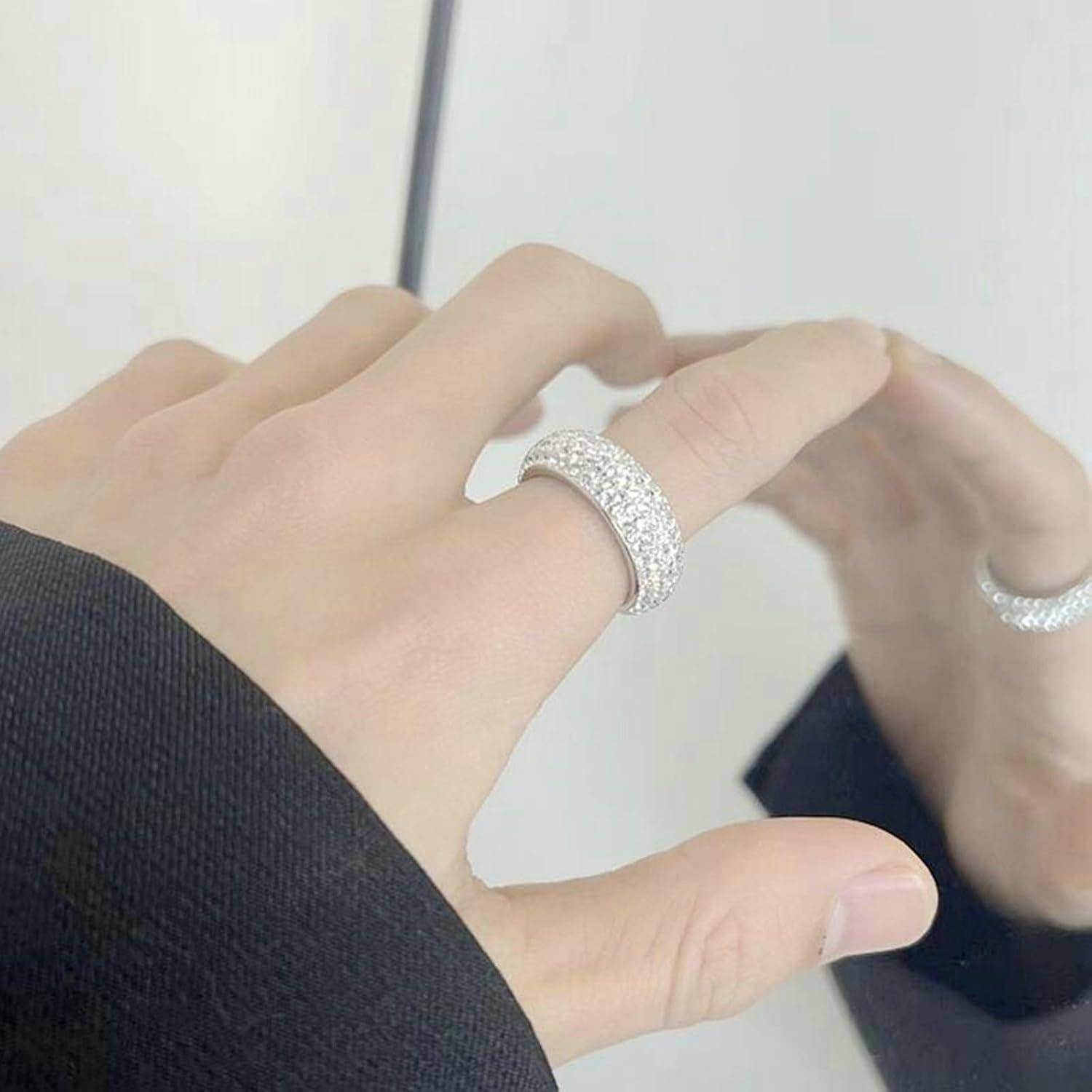 Eine Hand, die einen funkelnden Ring mit Reihen kleiner Diamanten trägt, teilweise in einem Spiegel reflektiert und dabei Eleganz und Stil einfängt.