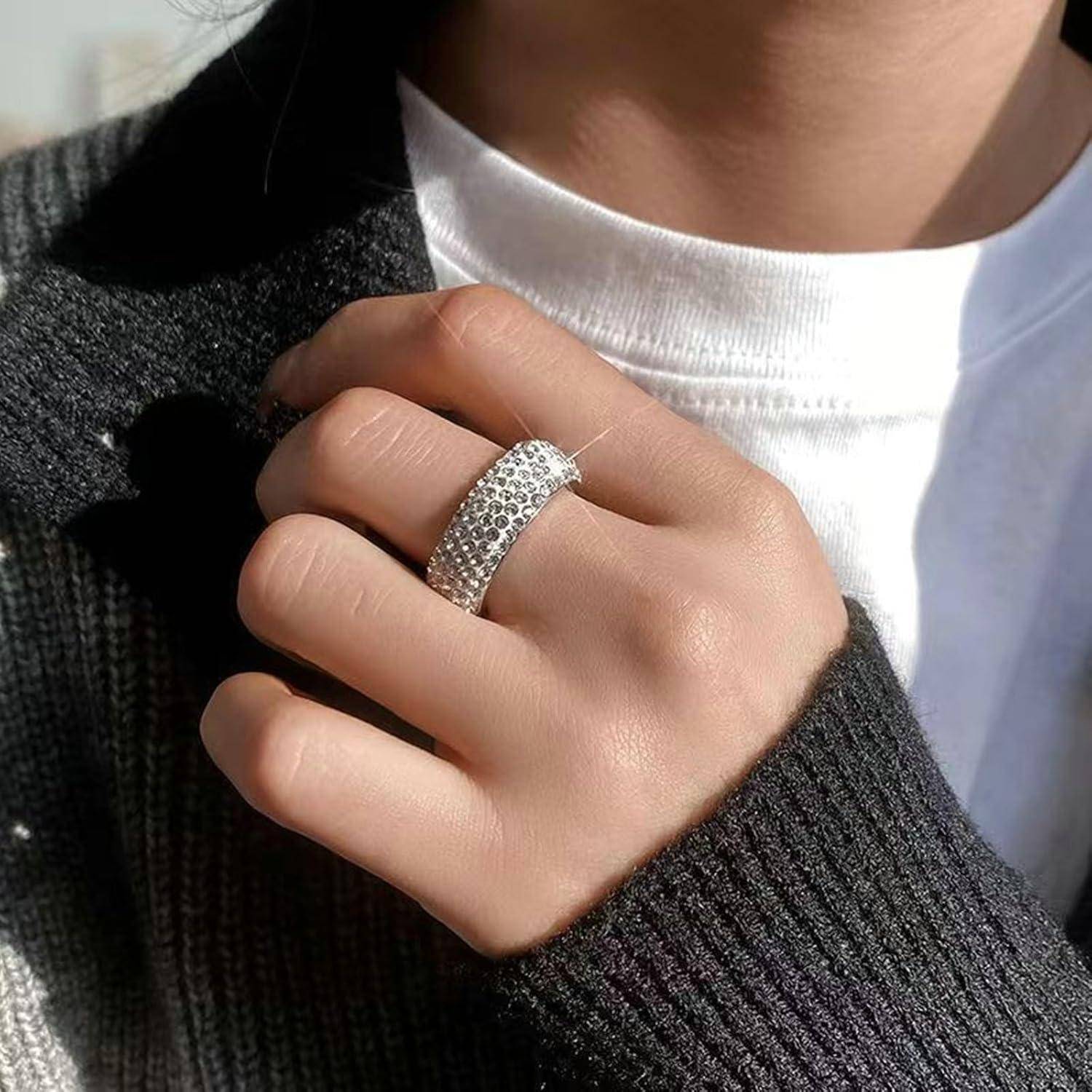 Eine Person trägt einen strukturierten silbernen Ring am Zeigefinger, über einem gerippten schwarzen Pullover und weißem T-Shirt, in natürlichem Licht.