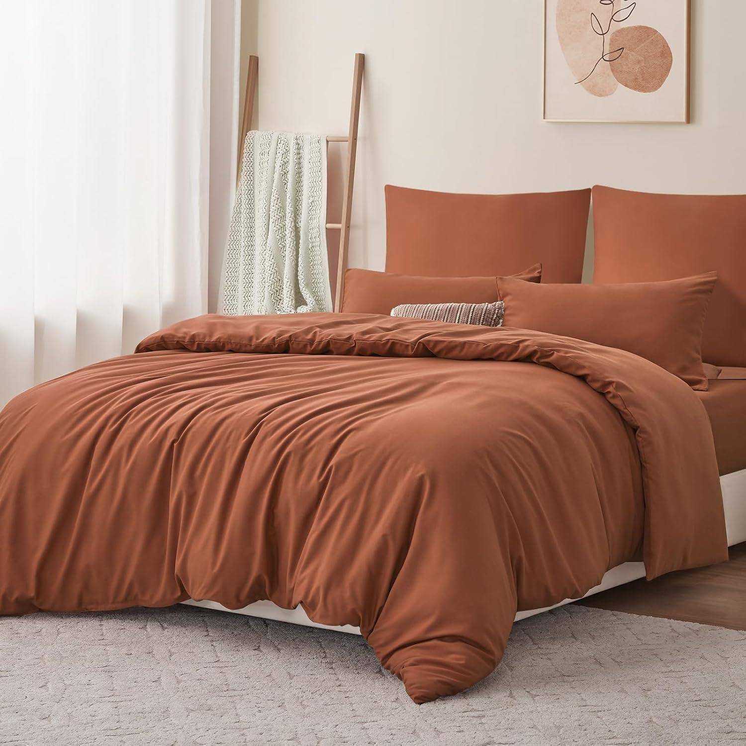 Ein Schlafzimmer mit einem sorgfältig gemachten Bett, das braune Bettwäsche und Kissen trägt. Ein zusammengelegtes Handtuch hängt an einer Holzleiter neben dem Bett.