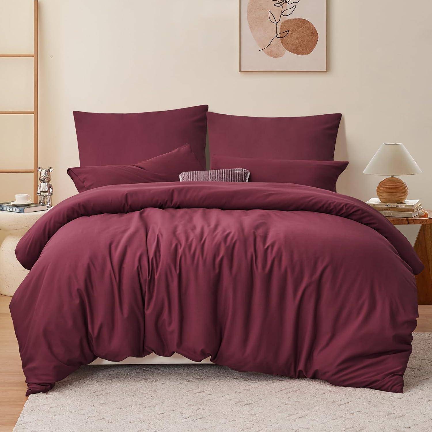 Ein ordentlich gemachtes Bett mit reichem Burgunderrot Bettwäsche, zwei großen Kissen und einer glatten Bettdecke. Ein minimalistisches Zimmer mit einer Lampe und neutraler Dekoration.