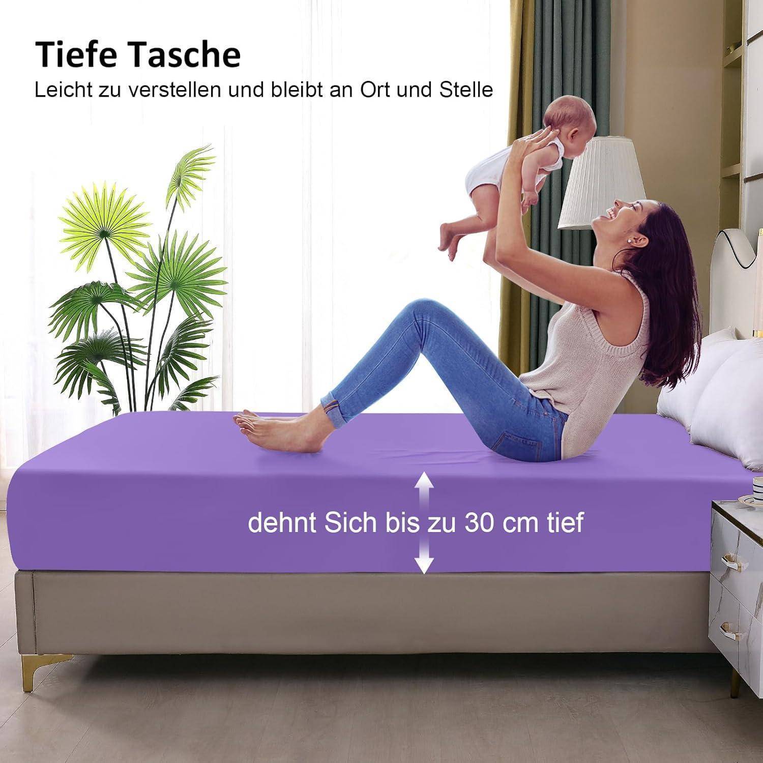Mutter sitzt auf einem lila Bett und hält ein Baby in der Luft, mit deutschem Text, der ein Spannbetttuch mit tiefer Tasche beschreibt, das sich bis zu 30 cm dehnt.
