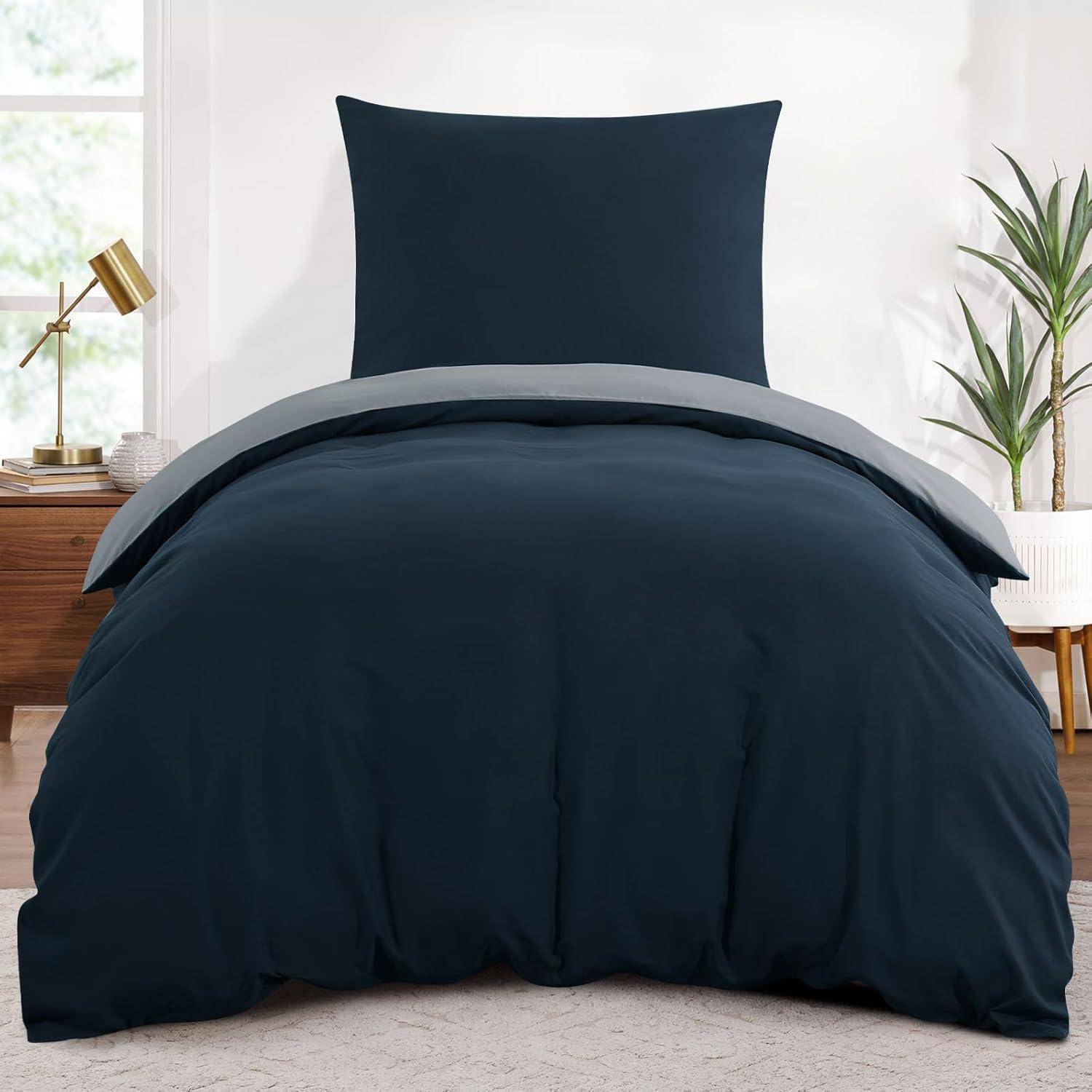 Ein ordentlich gemachtes Bett mit einem dunkelblau Bettüberwurf und passenden Kissen in einer modernen Schlafzimmereinrichtung mit einer kleinen Pflanze und einer Lampe in der Nähe.