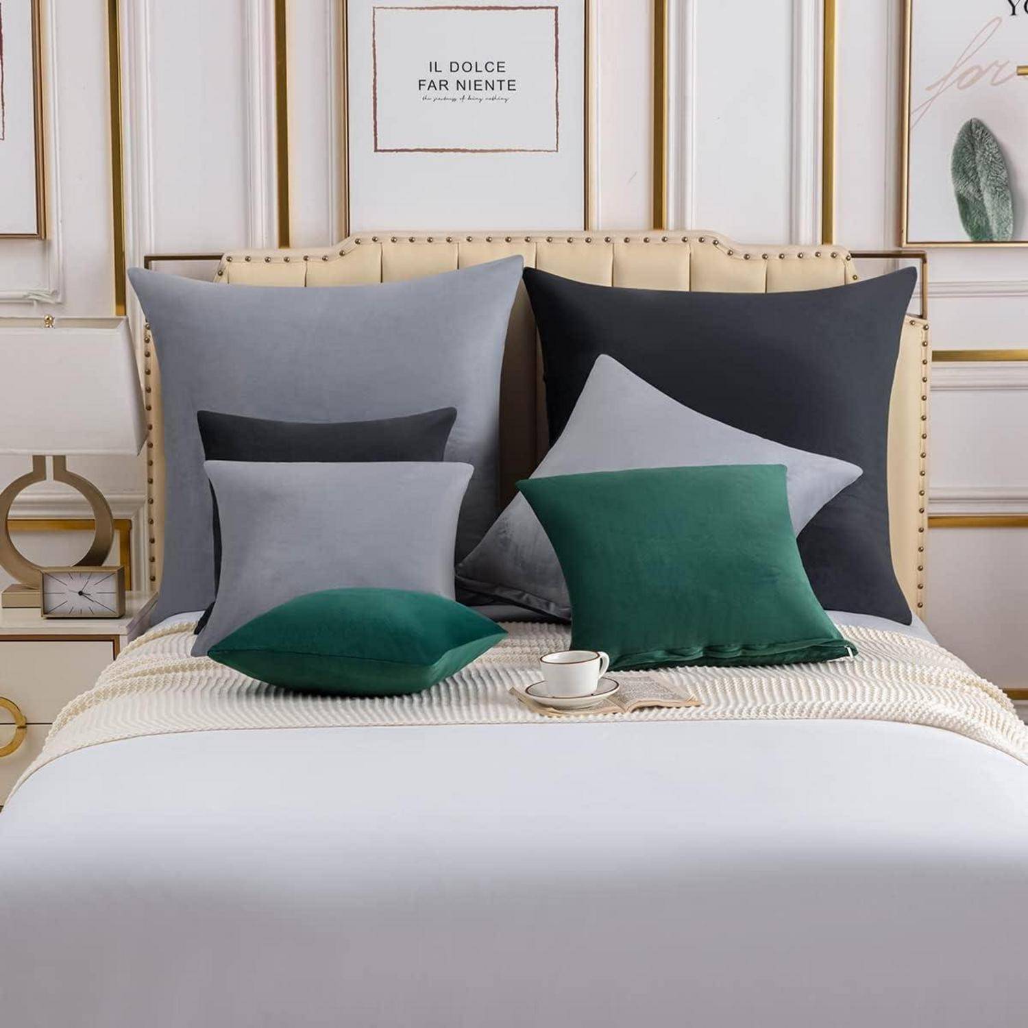 Ein ordentlich gemachtes Bett mit einer weißen Bettdecke, geschmückt mit verschiedenen grünen und grauen Kissen. Minimalistische Dekoration rahmt die Szene für einen modernen Look ein.