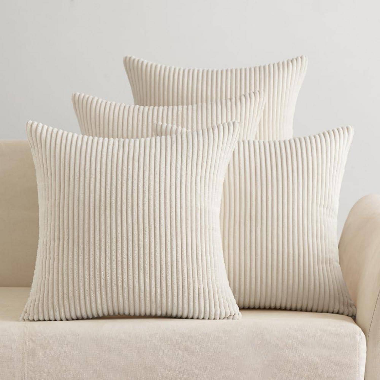 Vier weiße, geriffelte Kissen sind ordentlich auf einem cremefarbenen Sofa angeordnet und schaffen eine gemütliche und minimalistische Wohnzimmeratmosphäre.