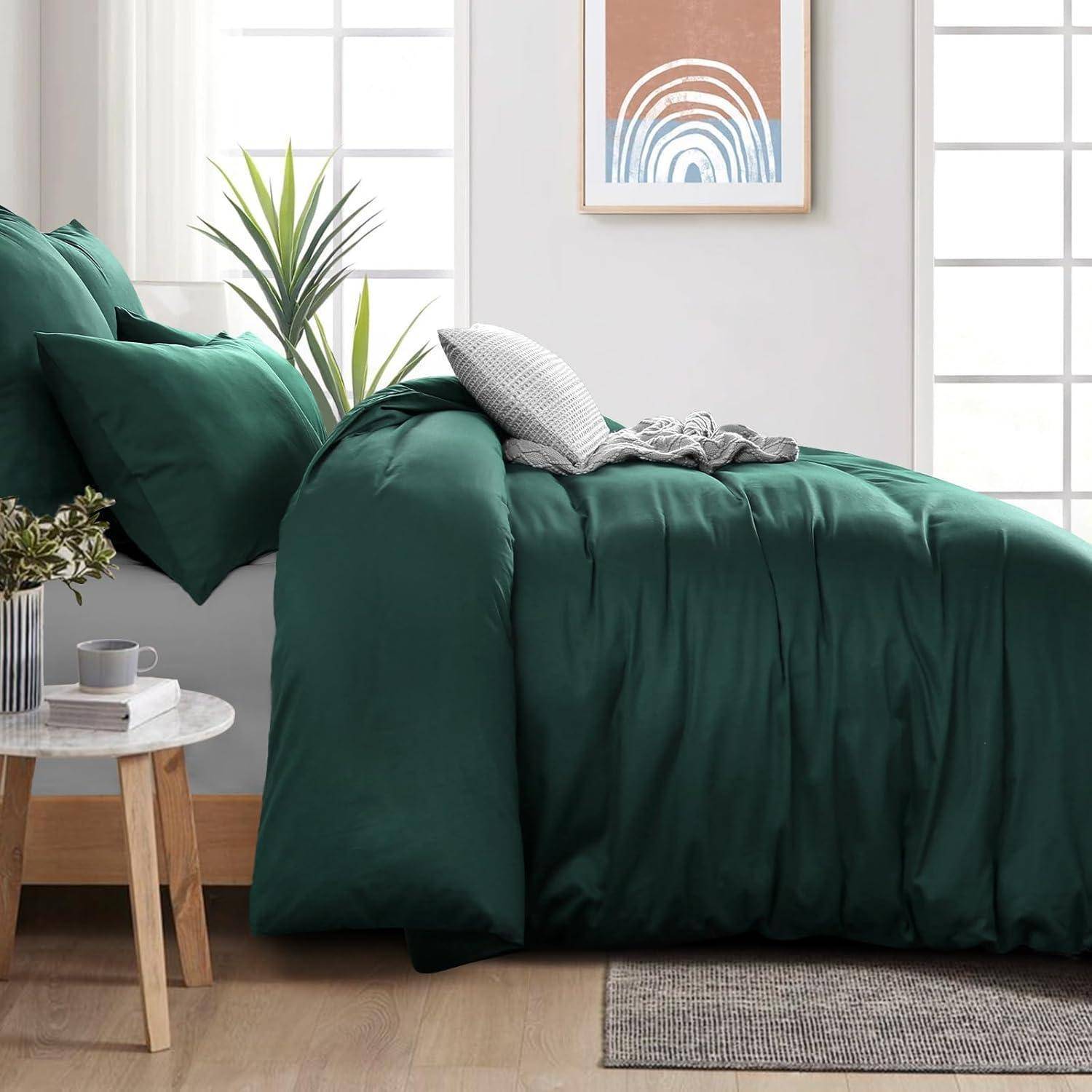 Ein ordentlich gemachtes Bett mit einer dunkelgrünen Bettdecke, mehreren Kissen und einem Nachttisch mit einer Pflanze und einer Tasse. Ein gerahmter abstrakter Druck hängt darüber.