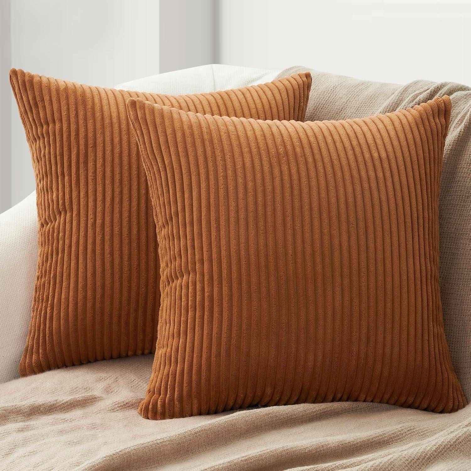 Zwei braune Cordkissen auf einer beigen Decke vor einer hellen Wand schaffen eine gemütliche und warme Atmosphäre in einem Wohnbereich.