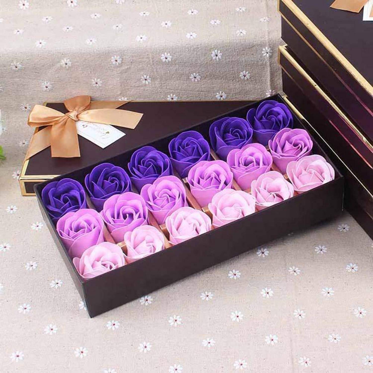 Eine schwarze Geschenkbox enthält rosenförmige Seifenblumen in Nuancen von Rosa und Violett. Ein goldenes Band und ein Geschenkanhänger zieren den geschlossenen Bereich.